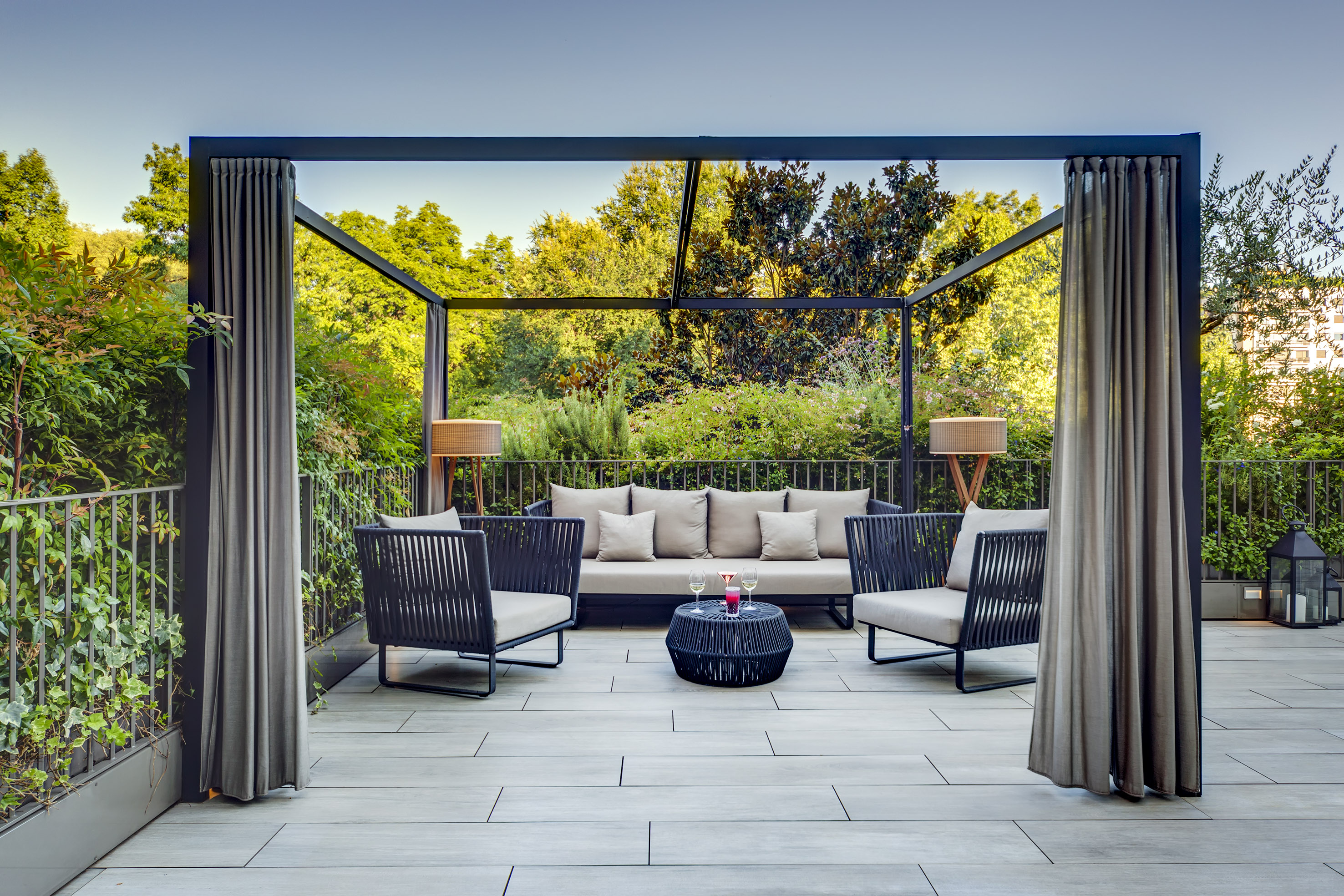 Outdoor patio lounge with modern furniture, pergola, and lush green garden.