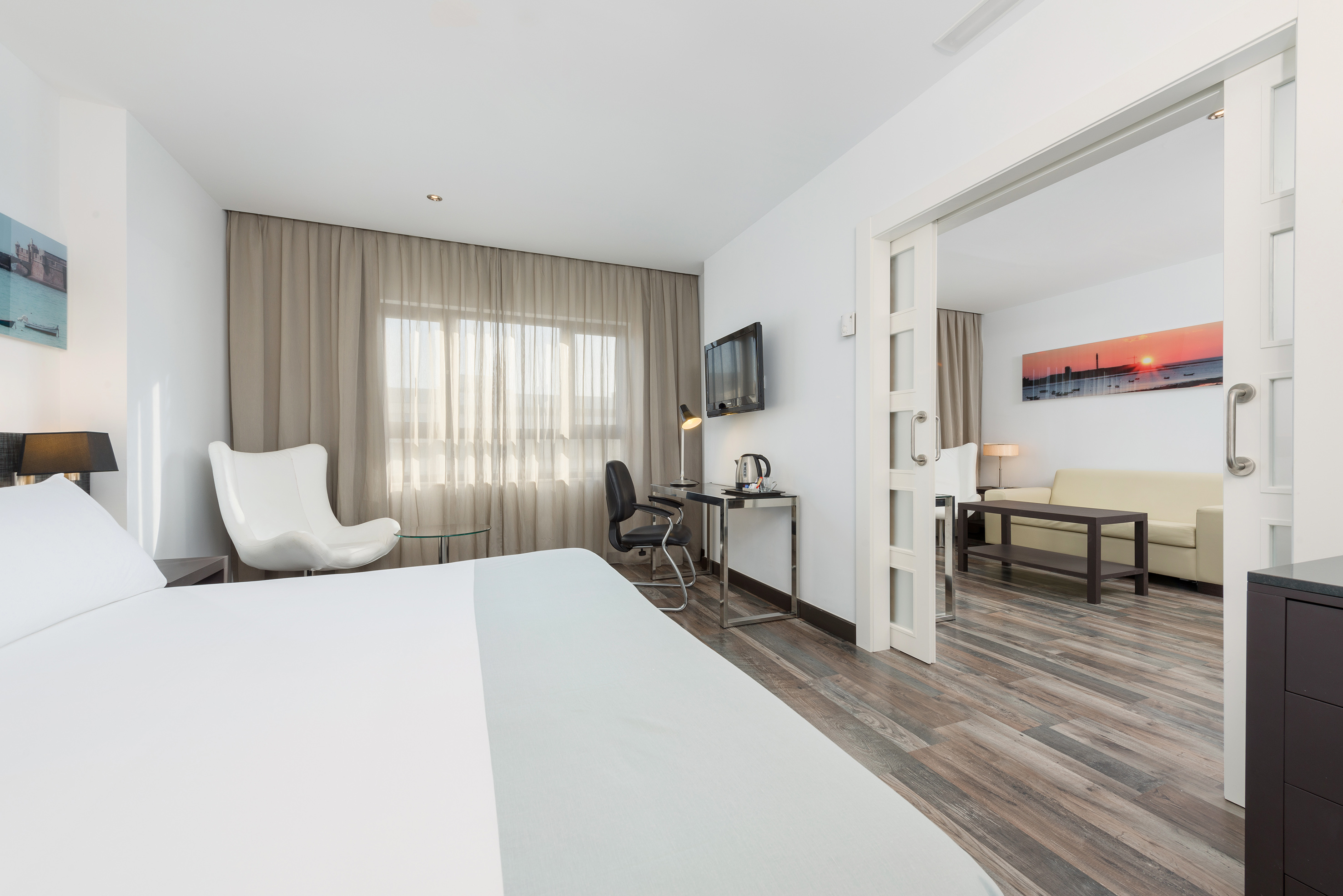 Hotel suite with modern bedroom, desk, TV, and connected living area.