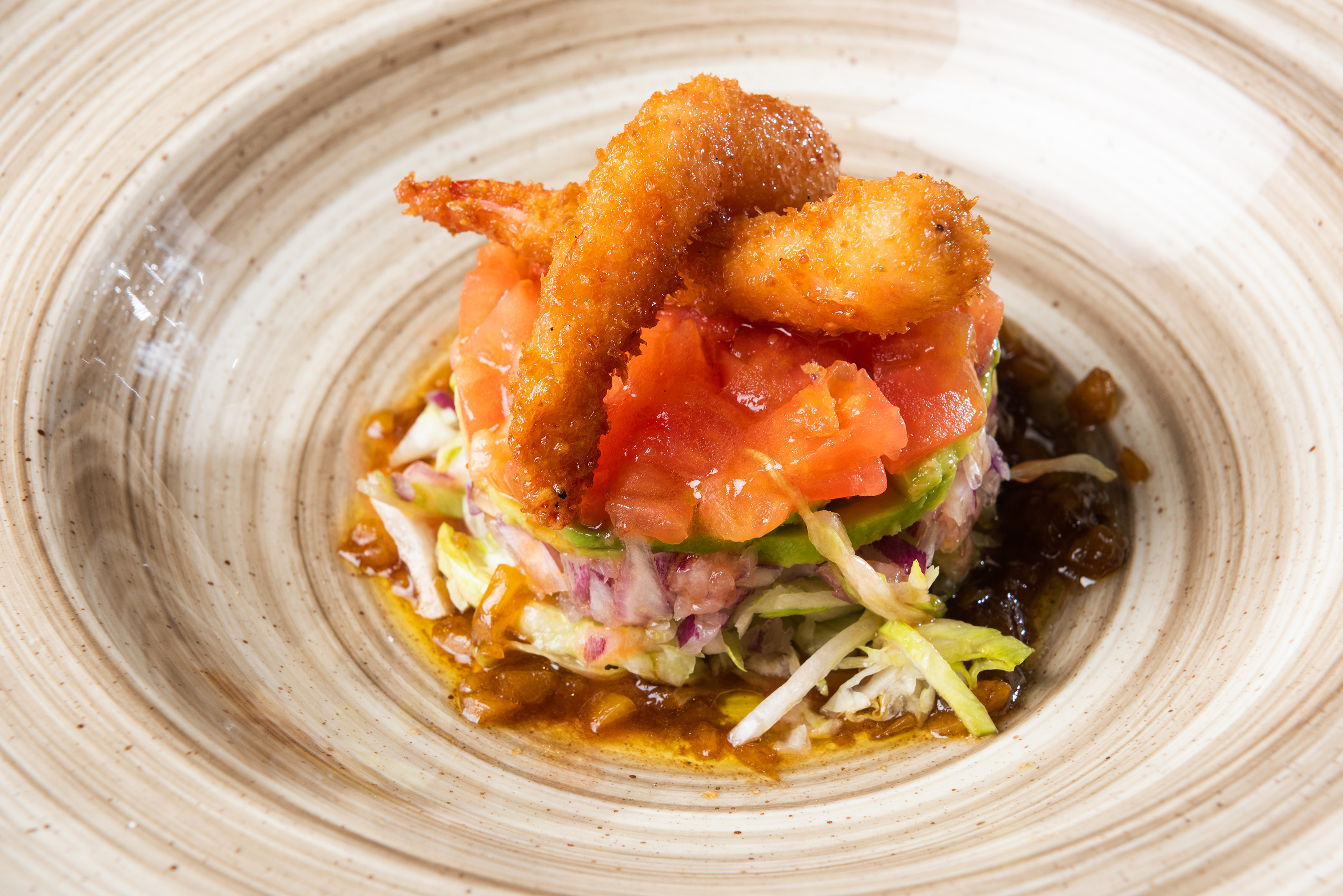 Fried shrimp appetizer layered with tomato, avocado, and red onion salad.