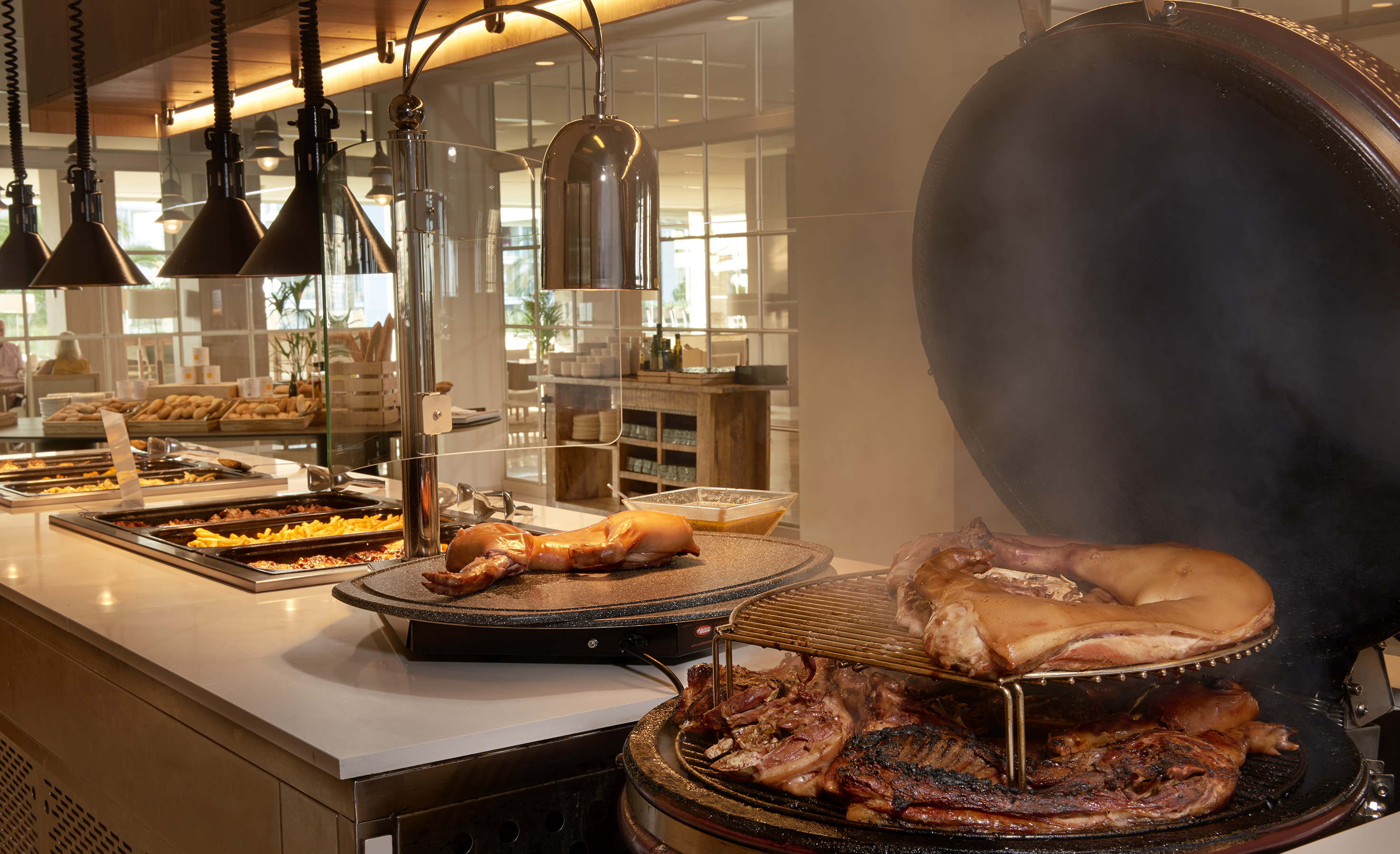 Smoking pork on kamado grill next to a hot buffet with carving station.