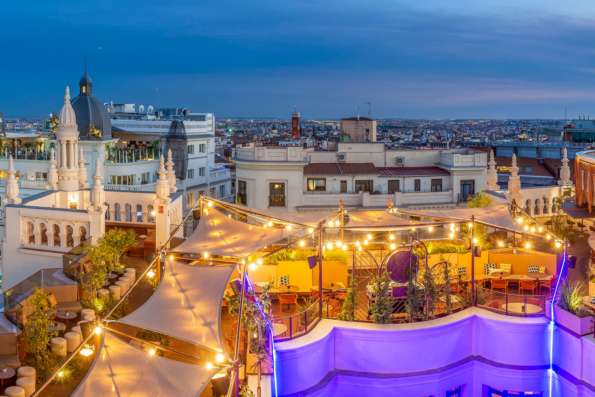 Madrid rooftop bar at dusk with string lights and city skyline view.