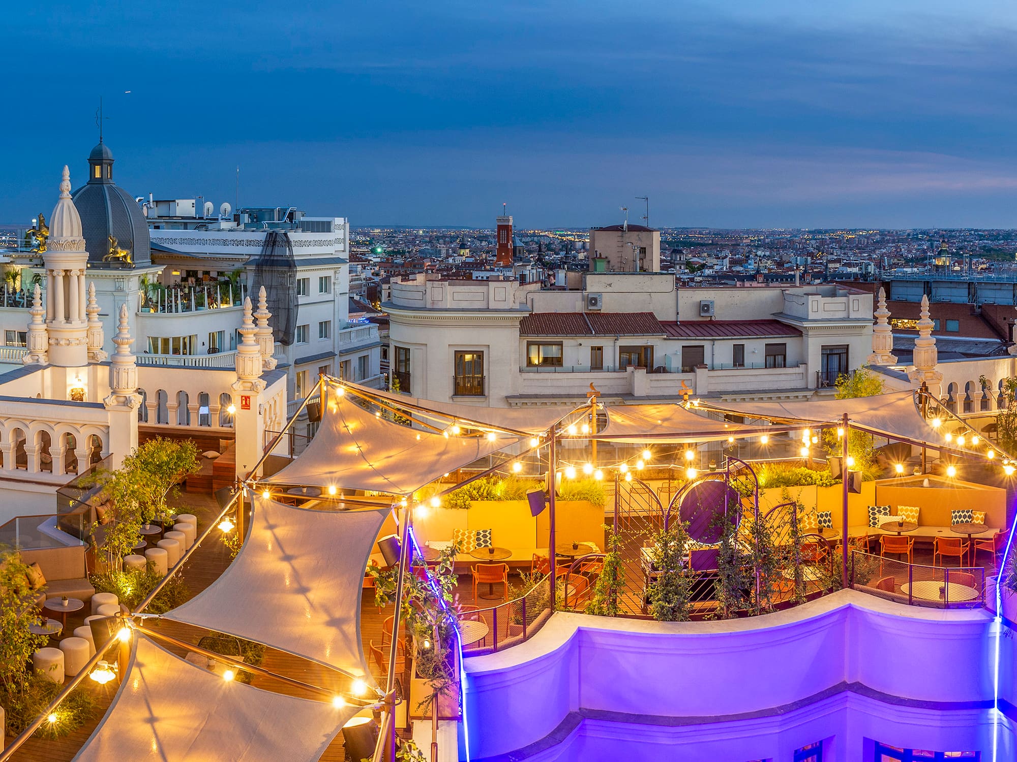 A rooftop patio adorned with lights, overlooking a bustling city skyline.