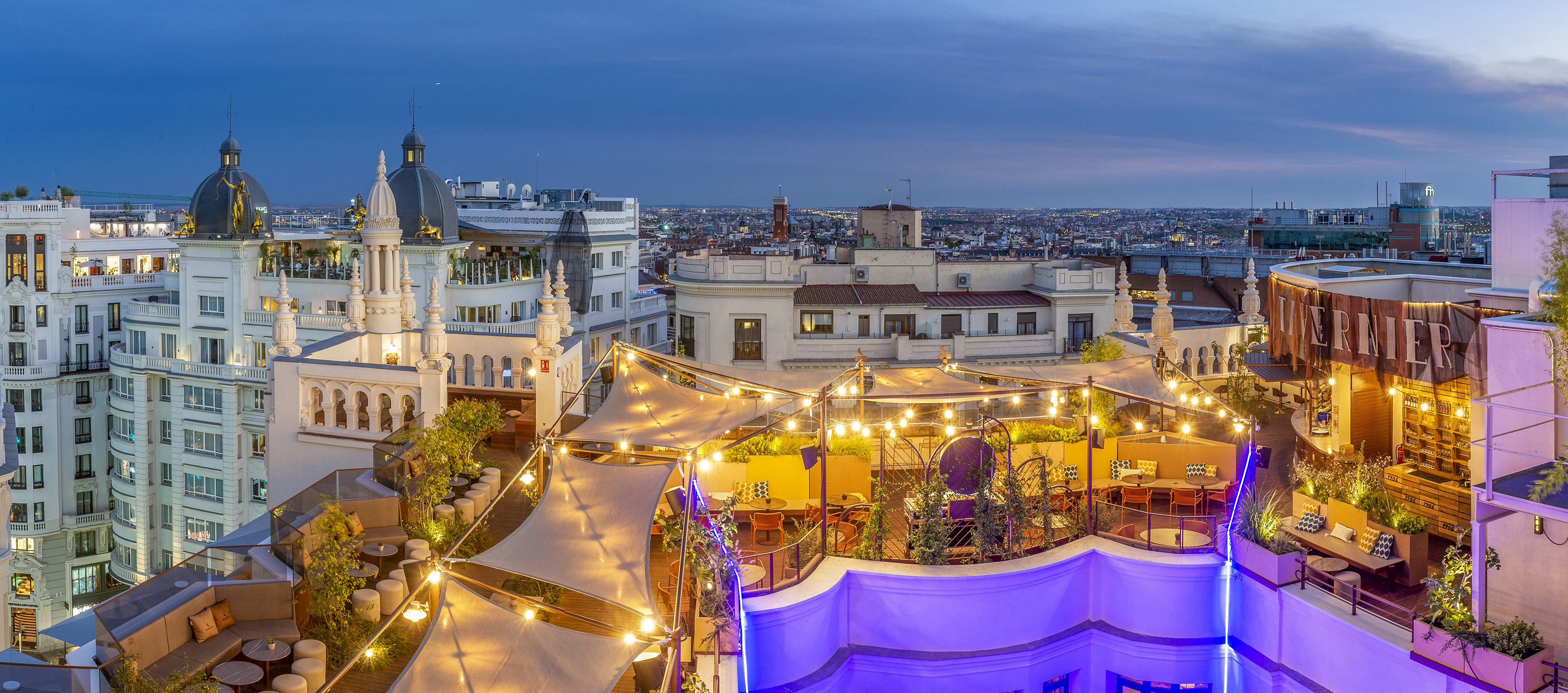 Madrid rooftop bar at dusk with string lights and city skyline view.