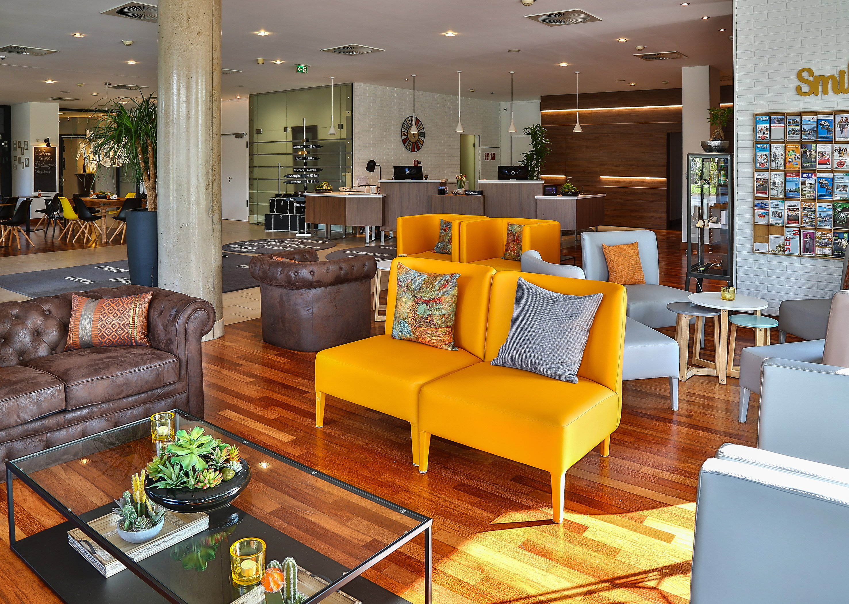 Modern hotel lobby lounge with yellow sofas, leather couch, and reception desk.