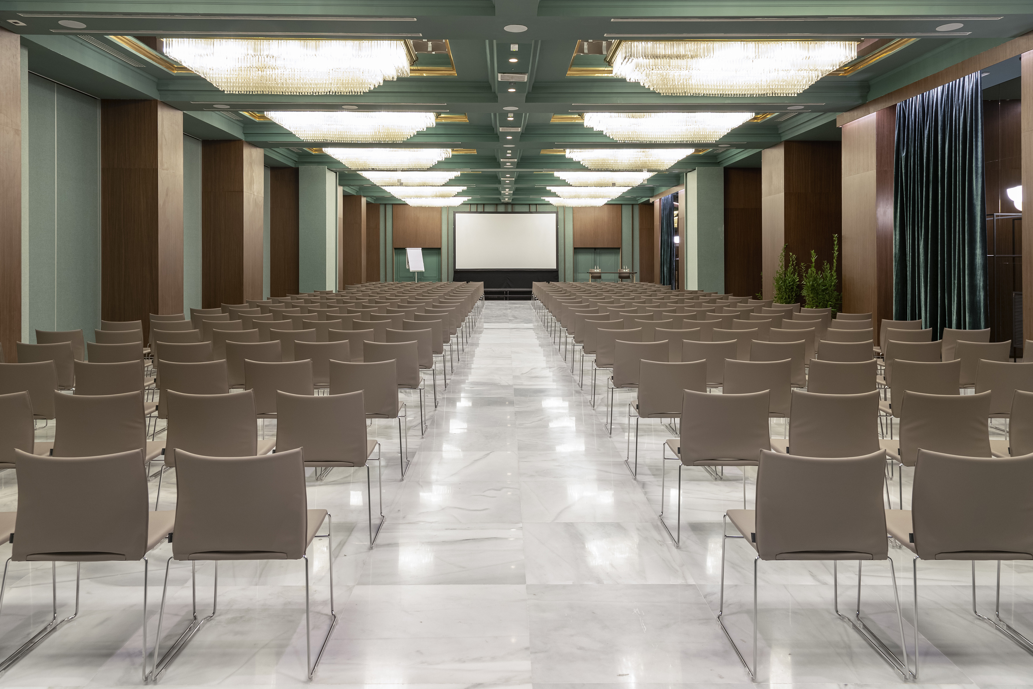 Luxurious empty conference hall with rows of chairs, screen, chandeliers.