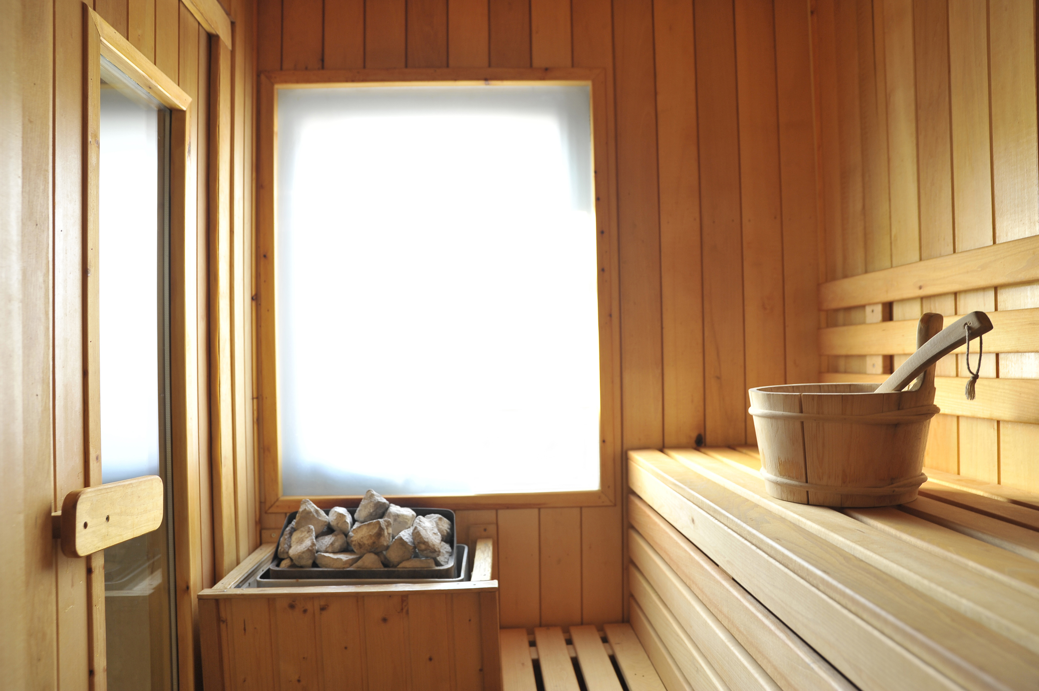 Wooden sauna interior with heater, rocks, bench, wooden bucket, and ladle.