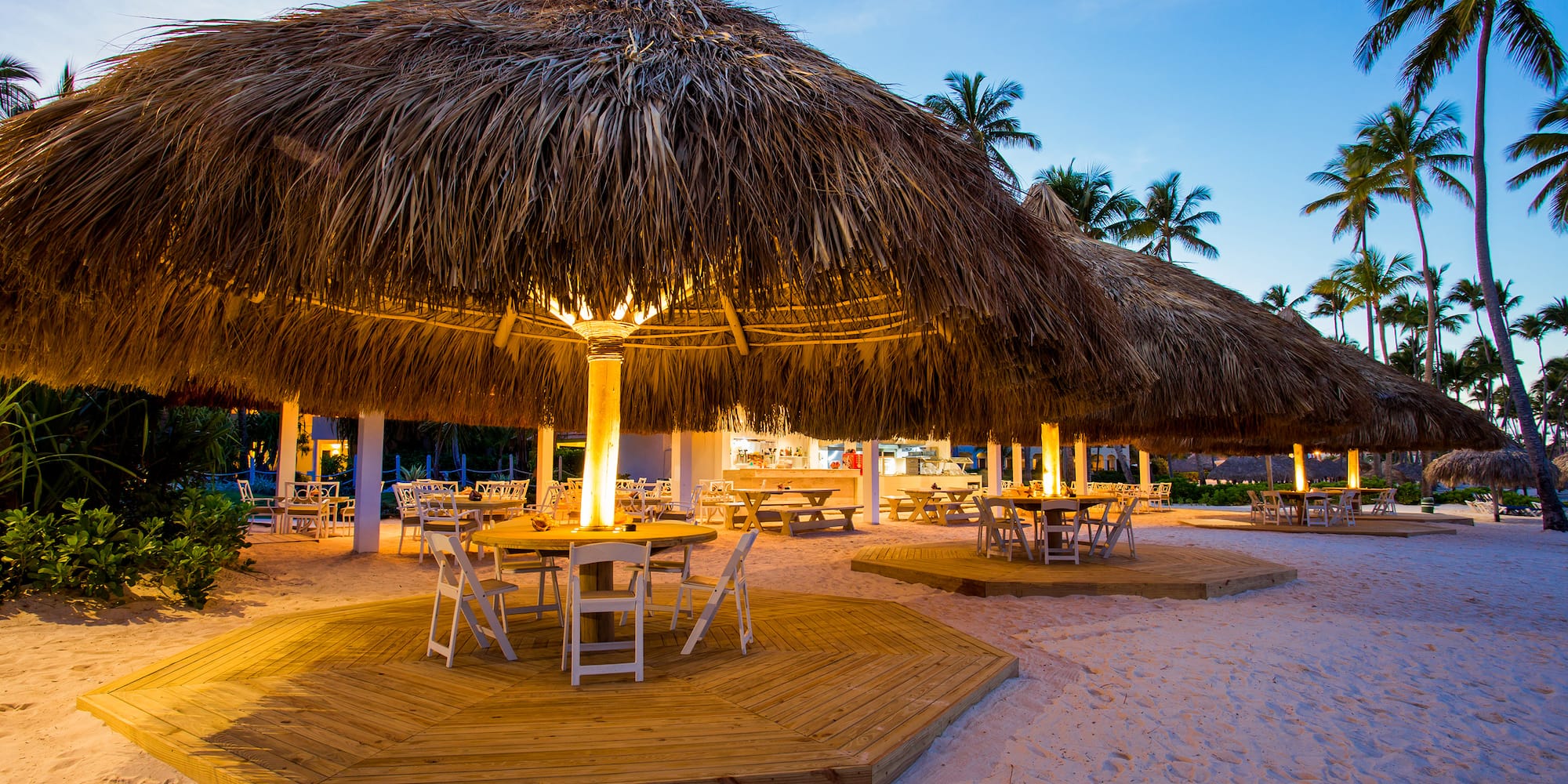 a group of tables and chairs under straw umbrellas on a beach