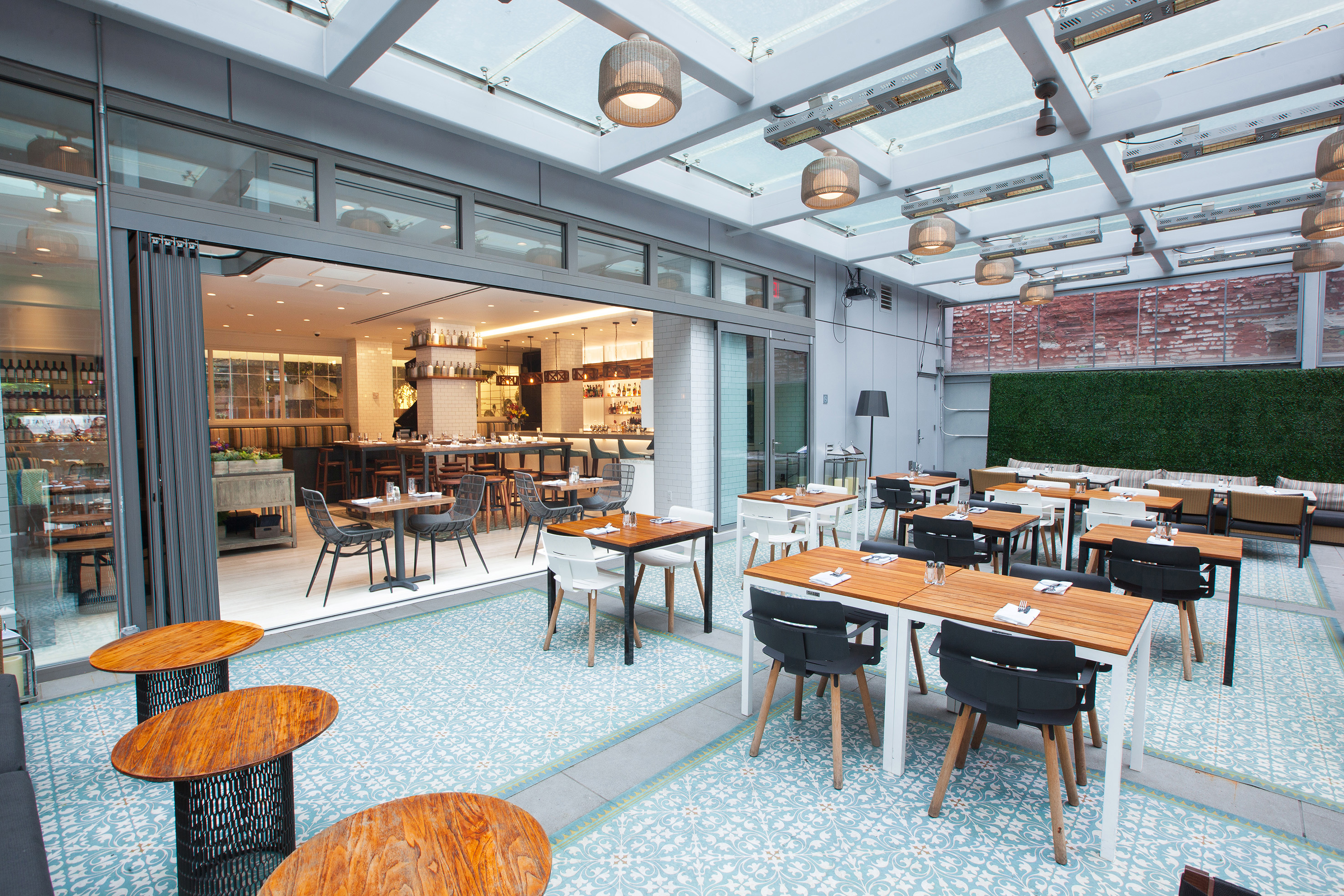 Modern restaurant patio with glass roof, tiled floor, and open bar.