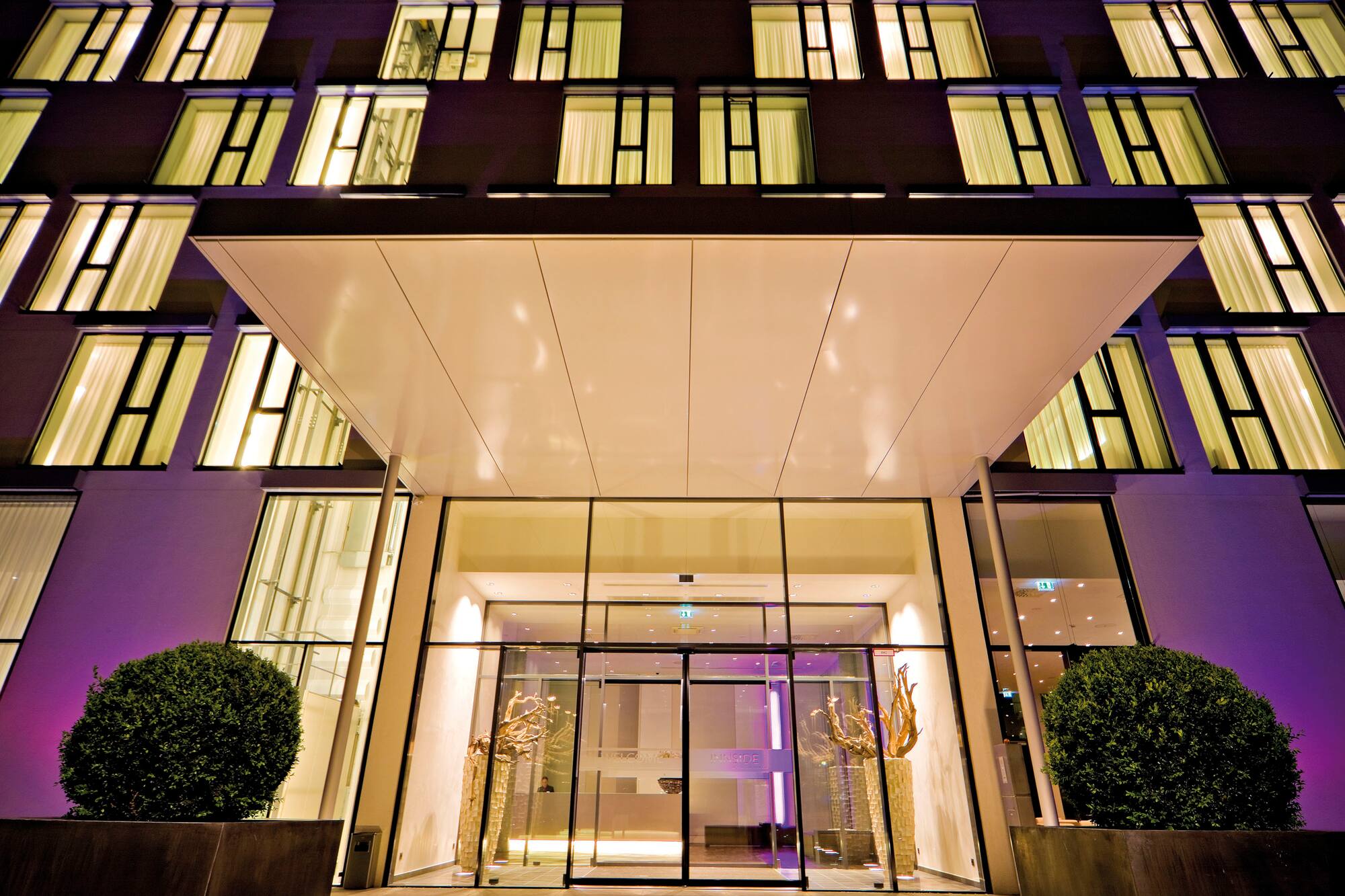 Modern hotel entrance at night, illuminated windows, building facade.