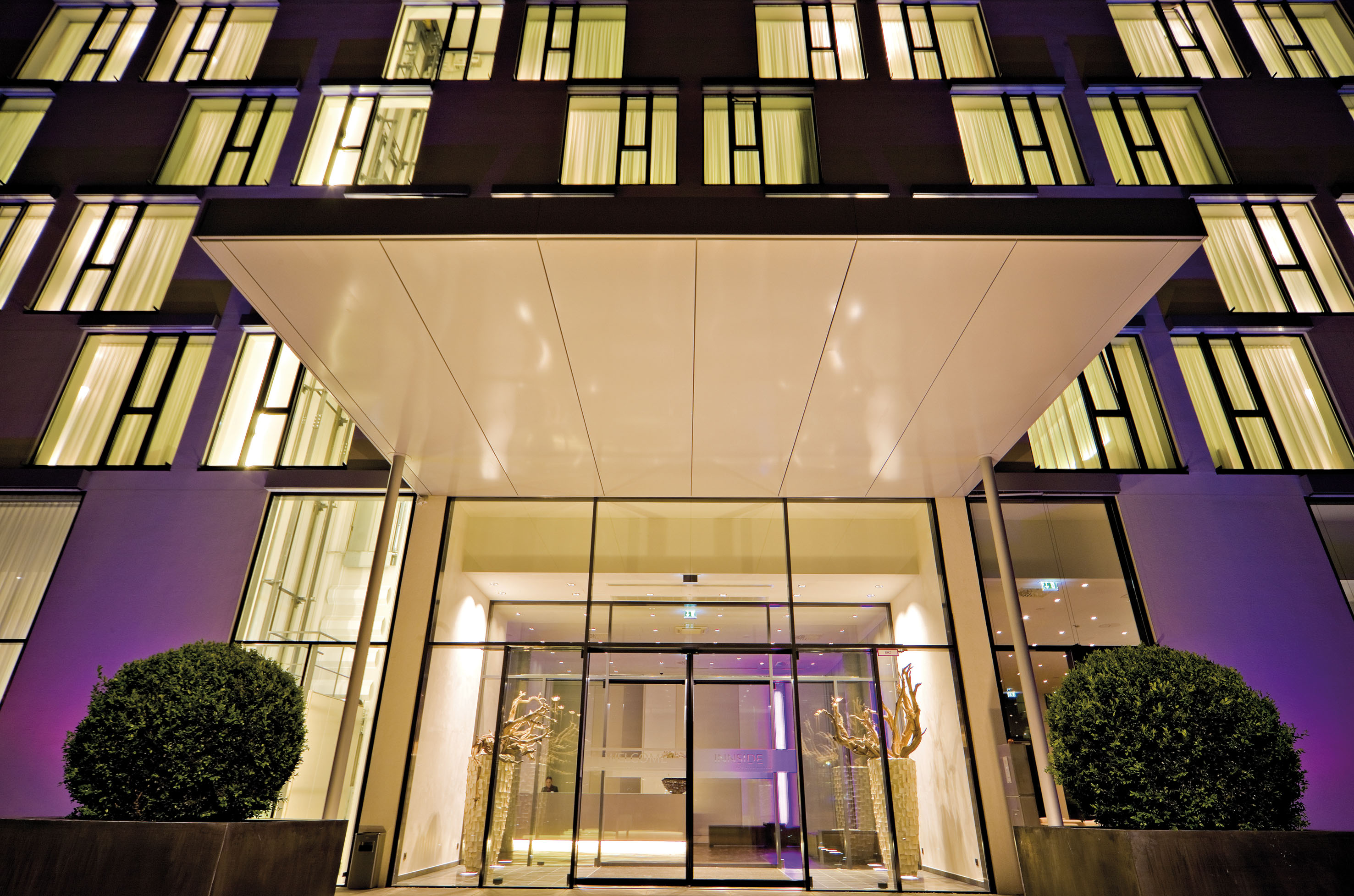 Modern hotel entrance at night, illuminated windows, building facade.
