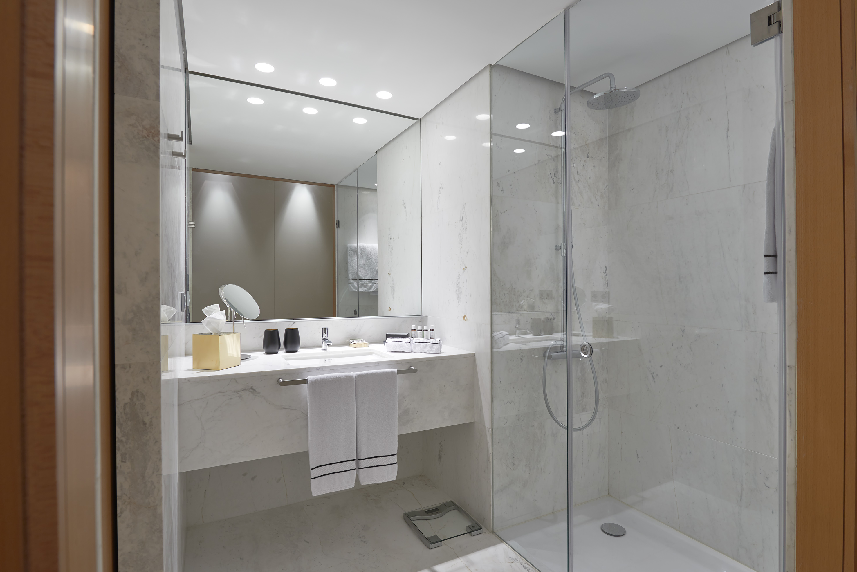 Modern hotel bathroom with marble vanity, mirror, and glass shower.