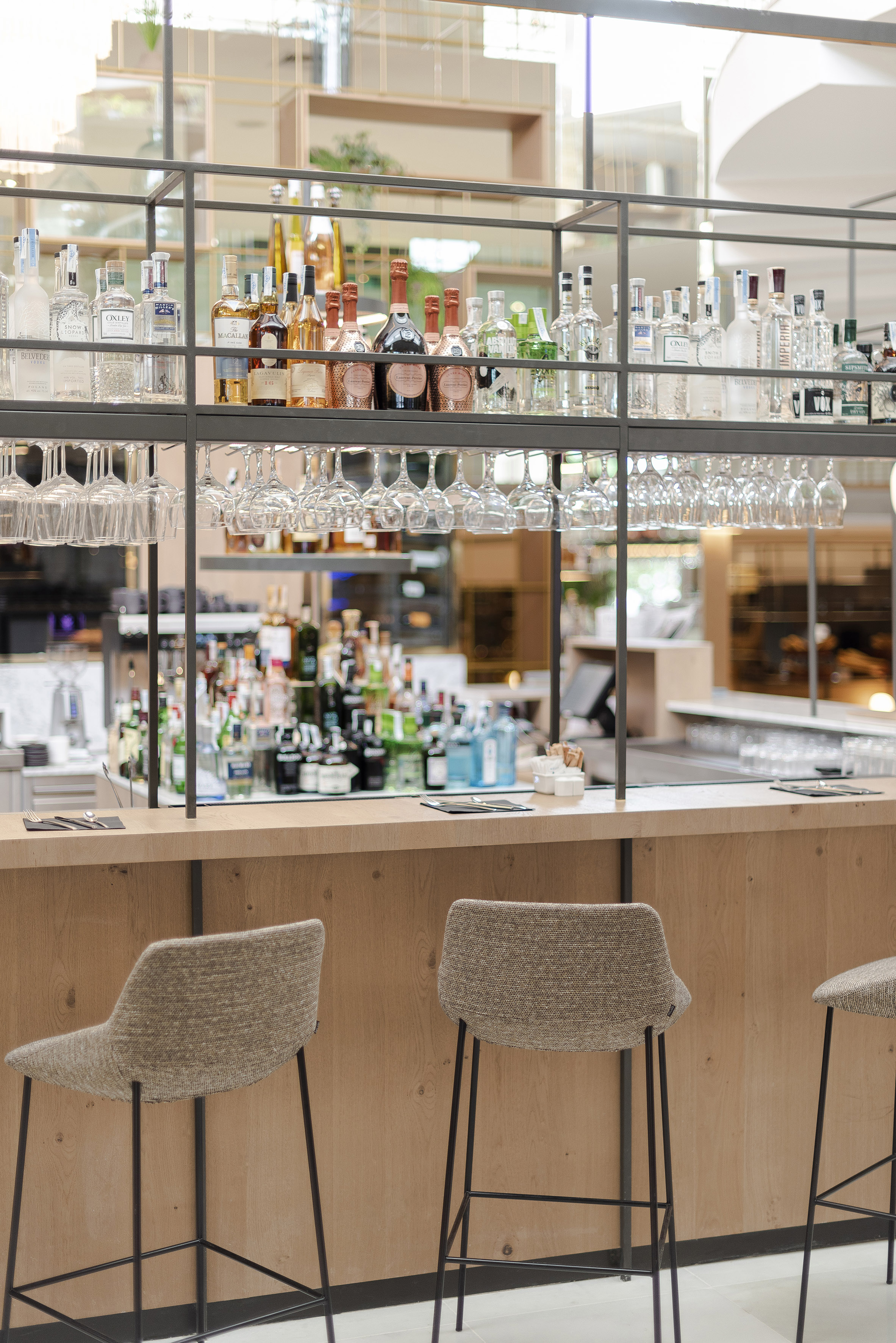 Modern hotel bar with liquor bottles, hanging glasses, and stylish bar stools.