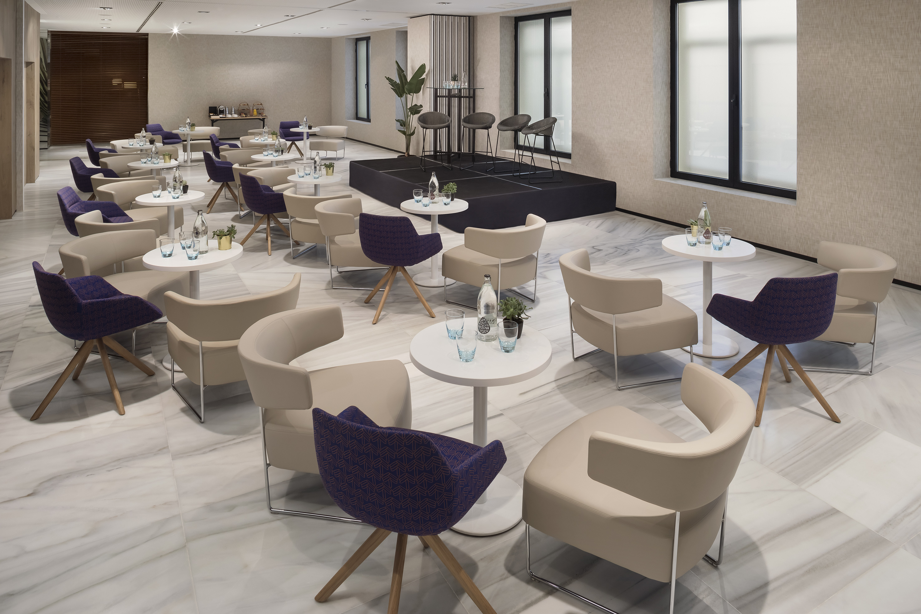 Modern conference lounge with mixed seating, small tables, stage, marble floor.