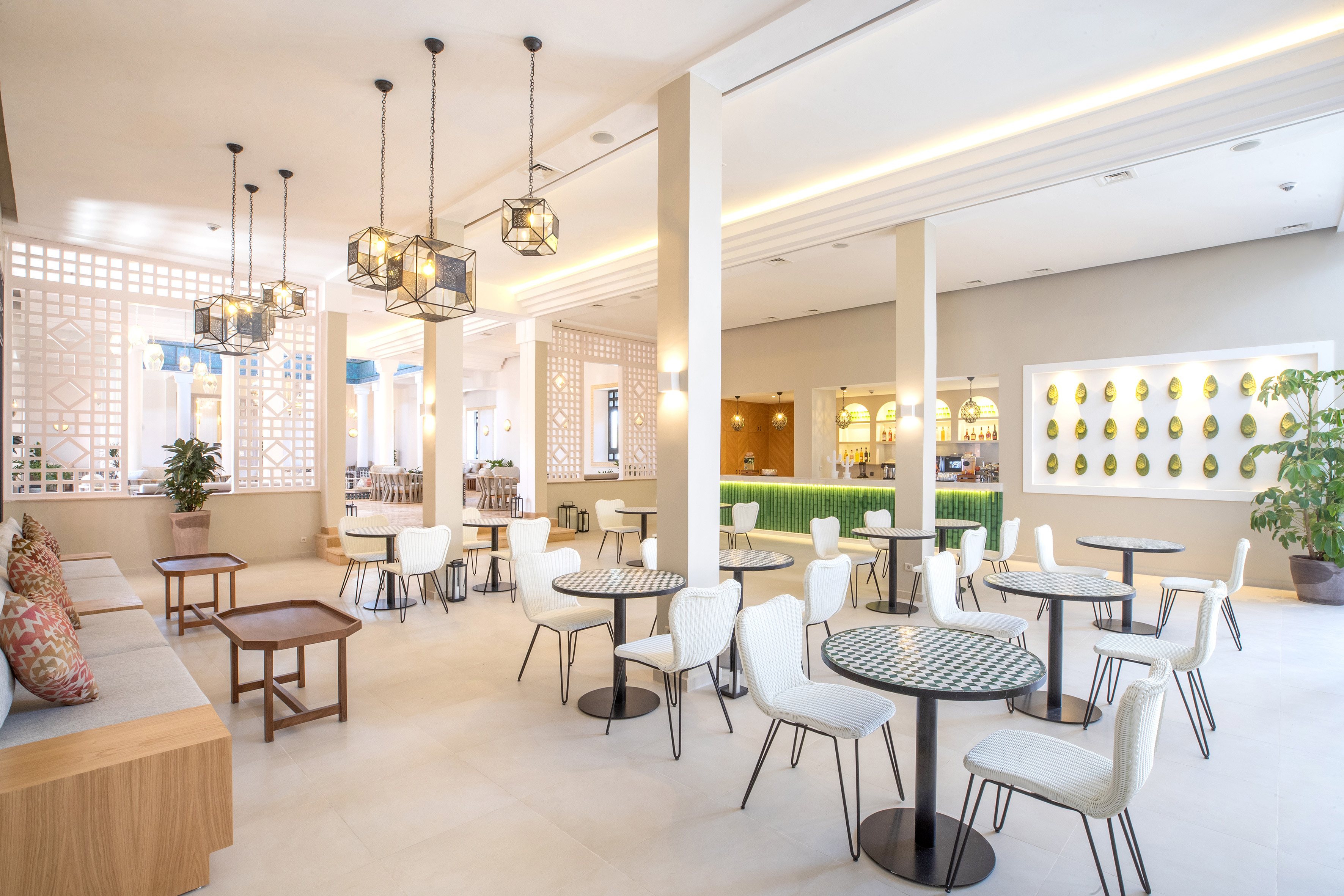 Modern hotel lounge with white chairs, mosaic tables, and a vibrant green bar.