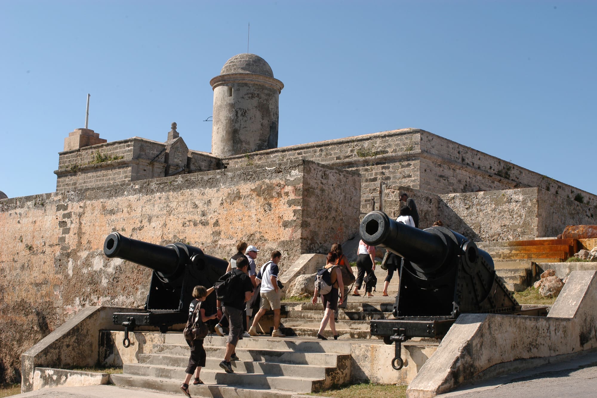 people walking up the stairs to a stone building with cannons