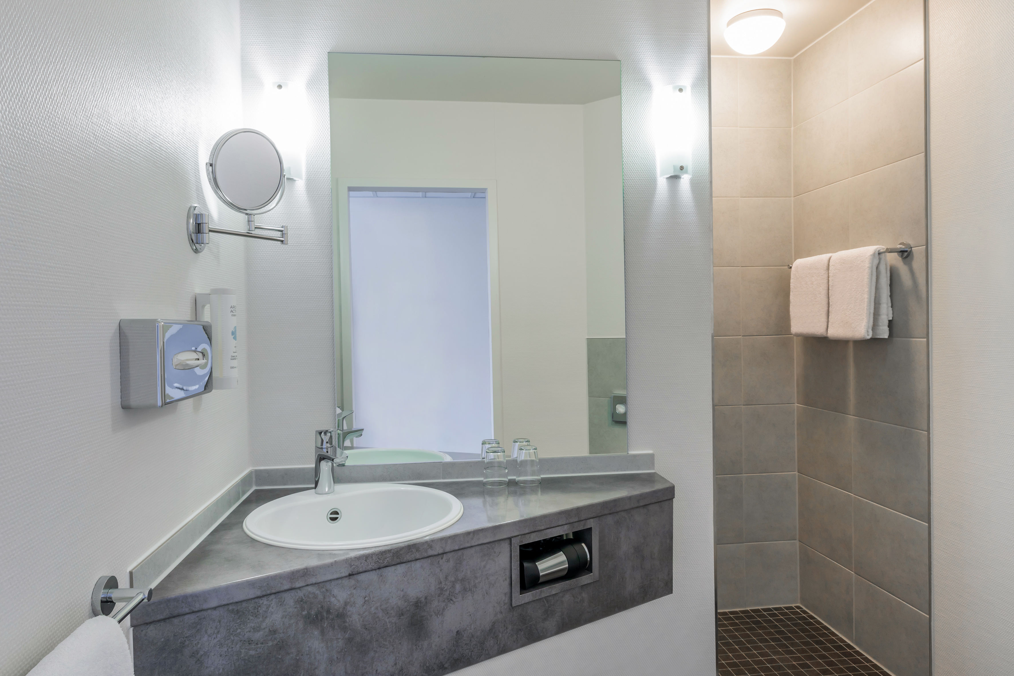 Modern hotel bathroom with sink, mirror, vanity, and tiled shower.