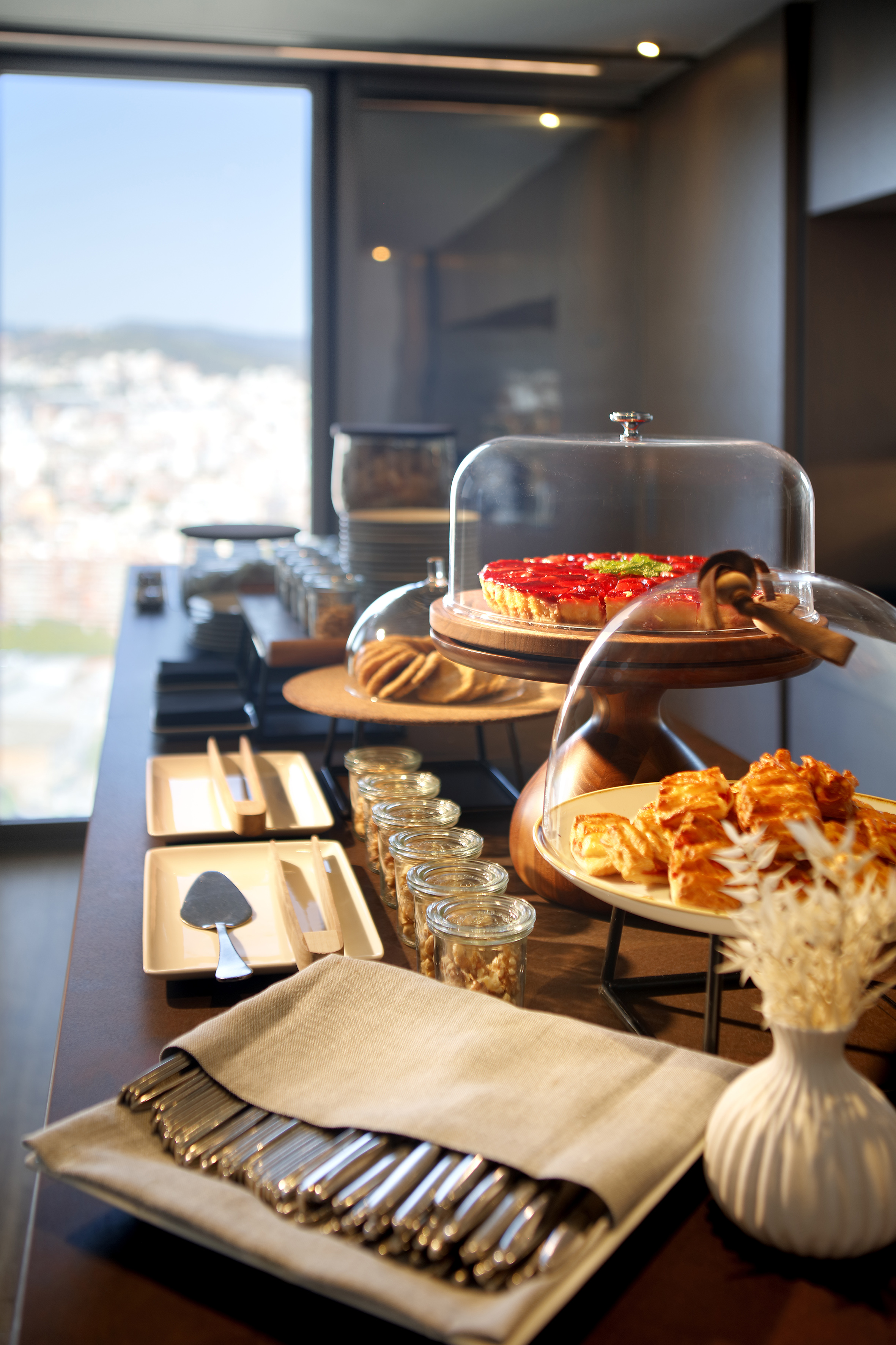 Elegant breakfast buffet with strawberry tart, pastries, nuts, and city view.