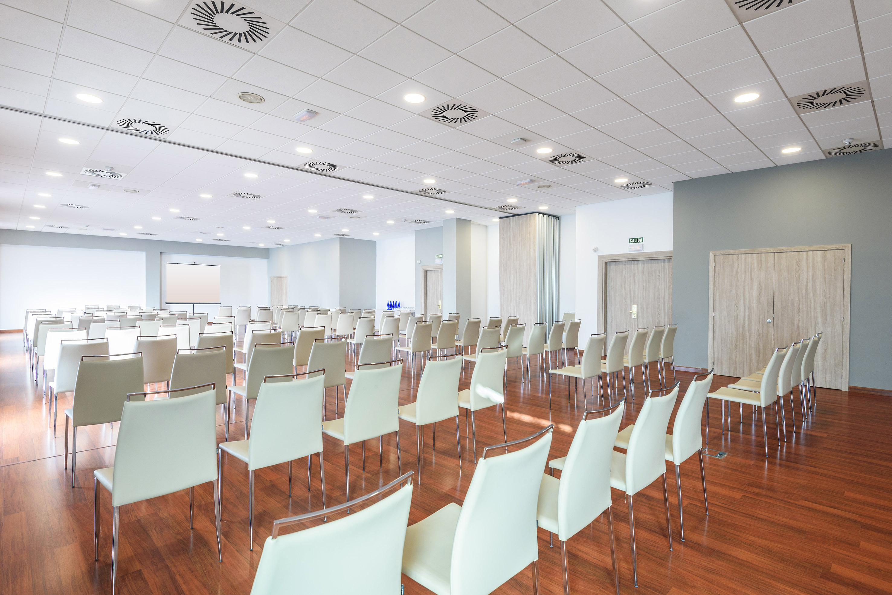 Modern meeting room with white chairs, projector screen, and wooden floor.