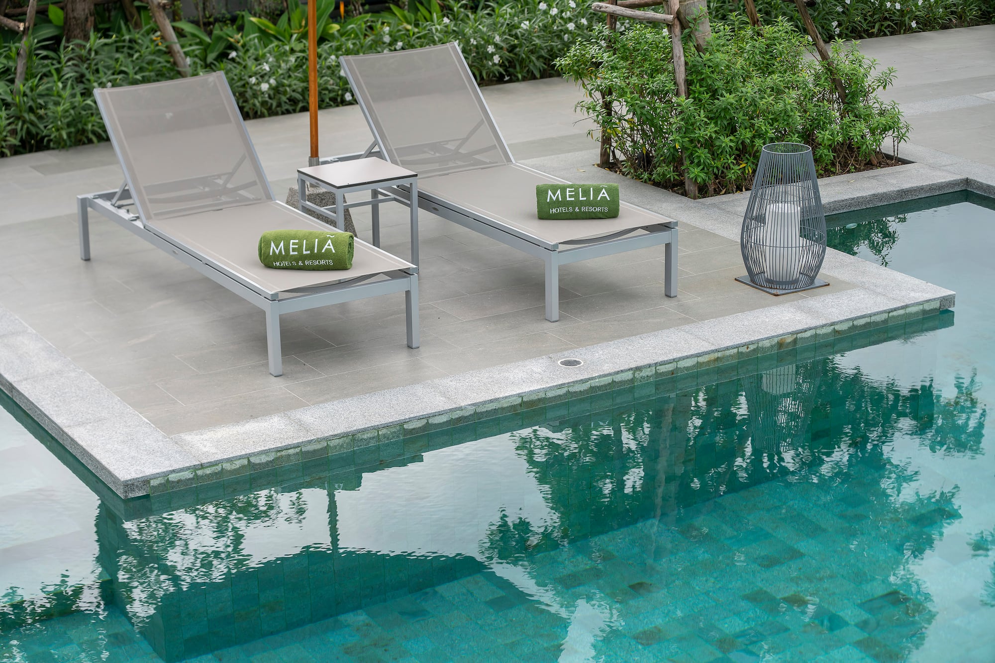 Meliã resort poolside with two gray sun loungers and green branded towels.