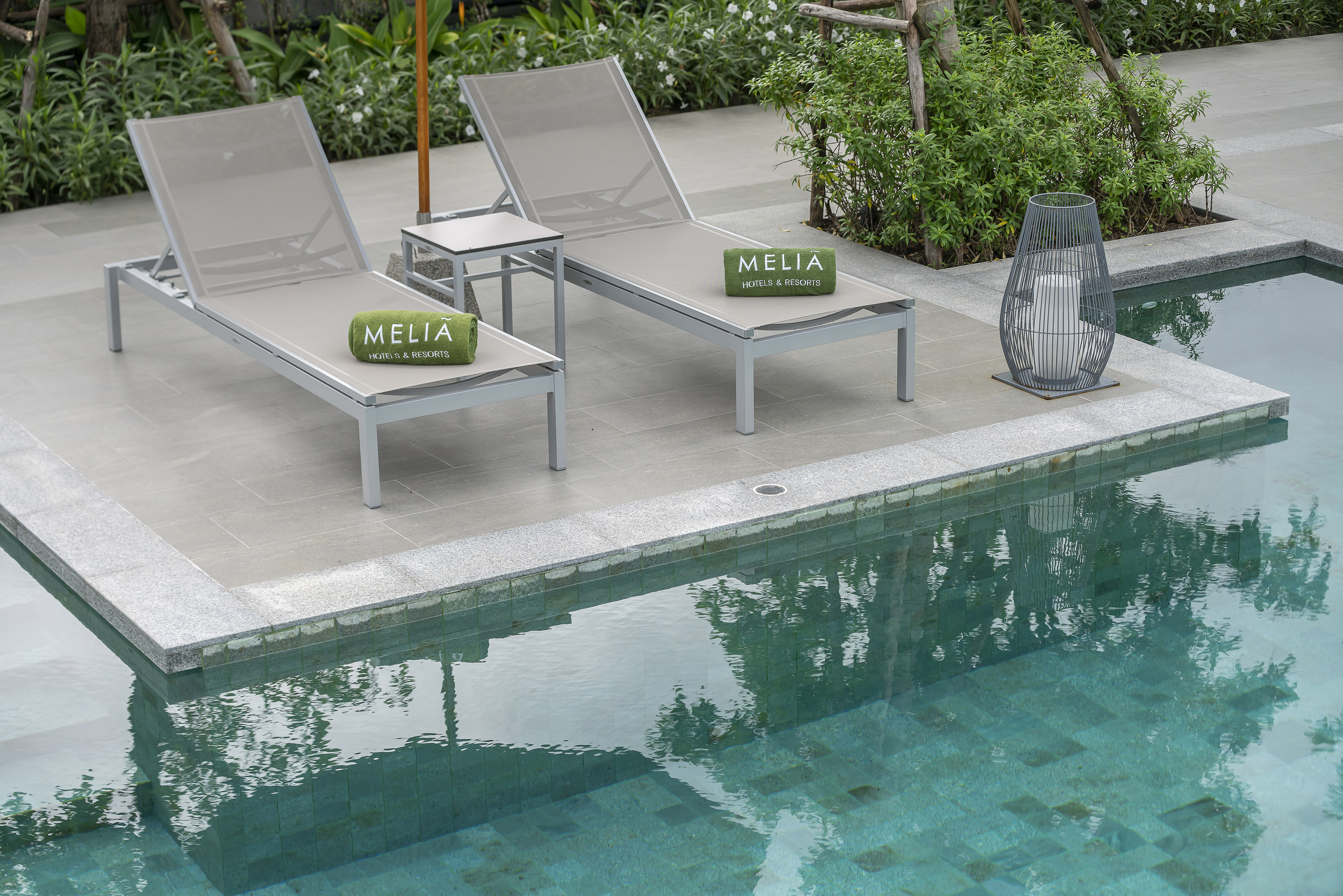 Meliã resort poolside with two gray sun loungers and green branded towels.