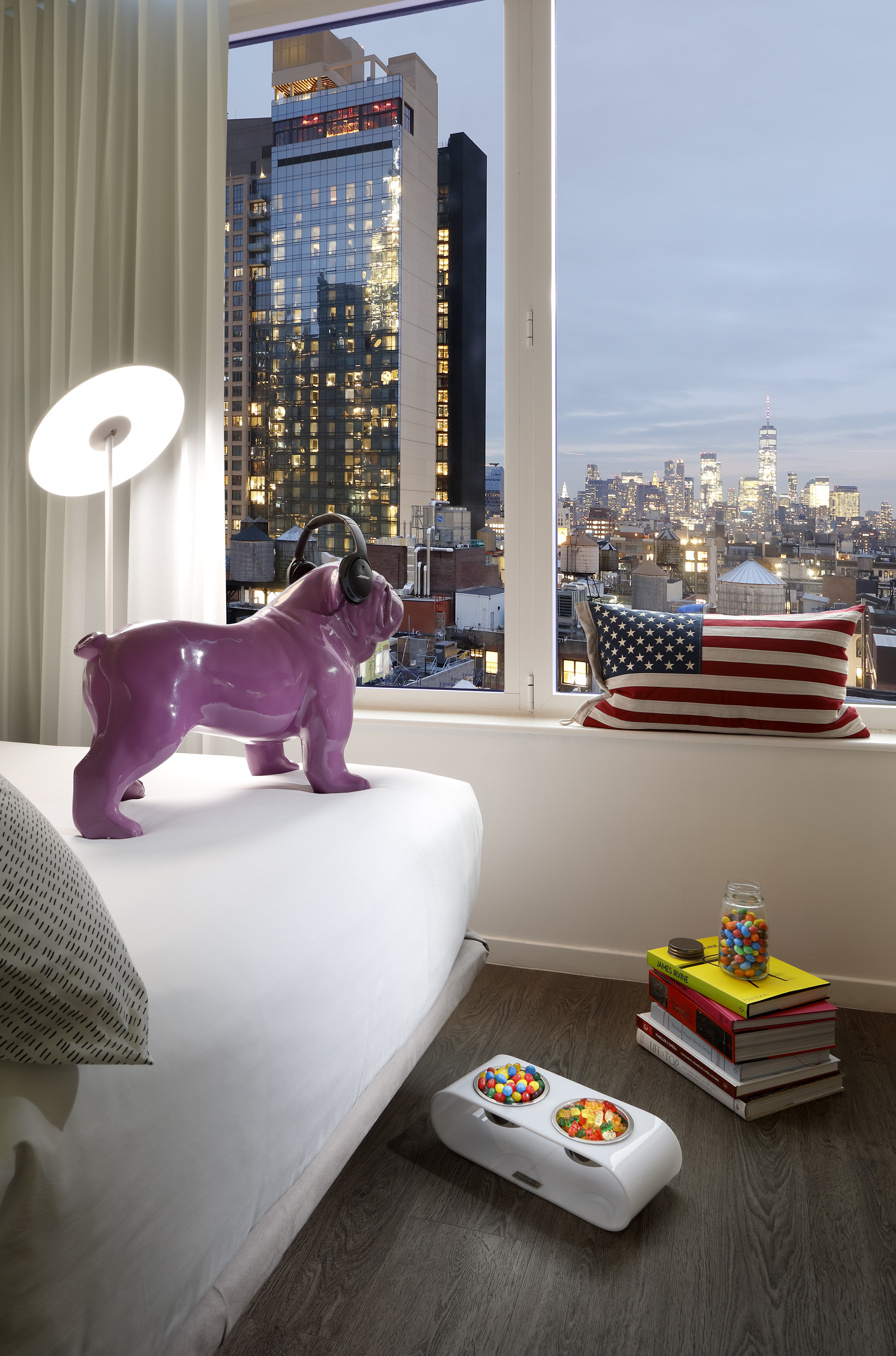 Purple bulldog statue with headphones in modern hotel room, NYC skyline view.