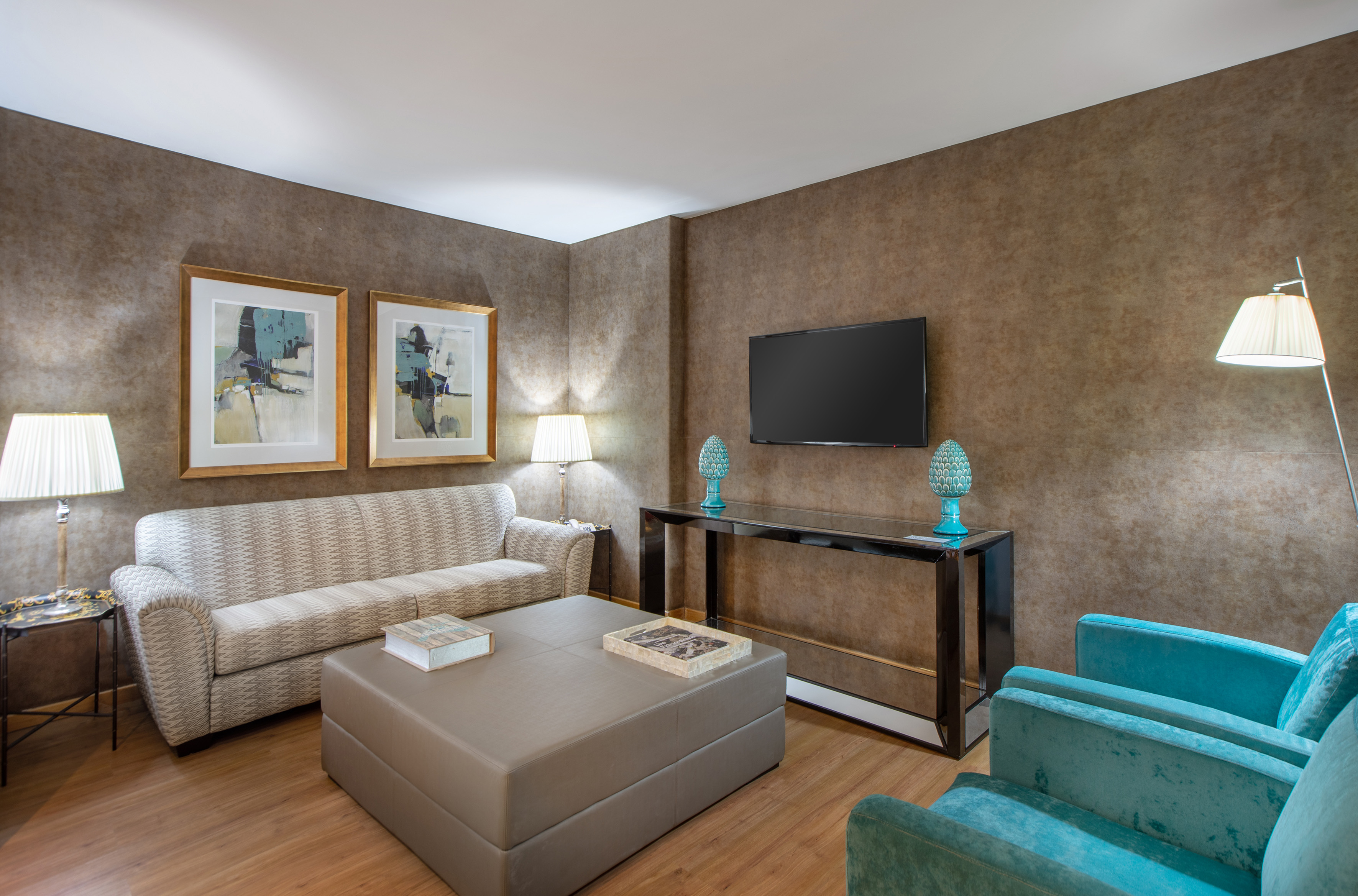 Living room with patterned sofa, teal armchairs, coffee table, TV, and art.