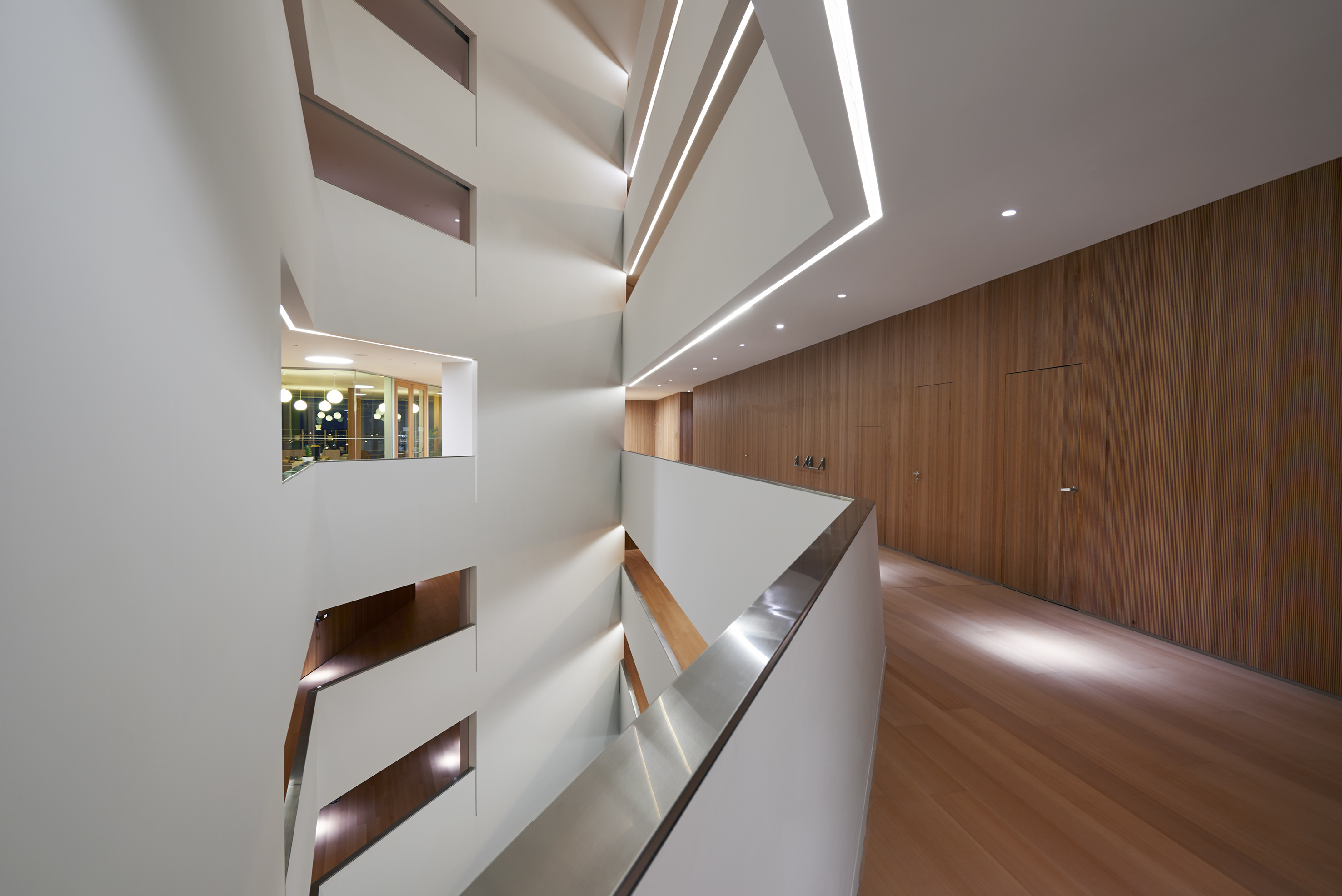 Modern architectural space with white walls, linear lighting, wood, and steel railing.