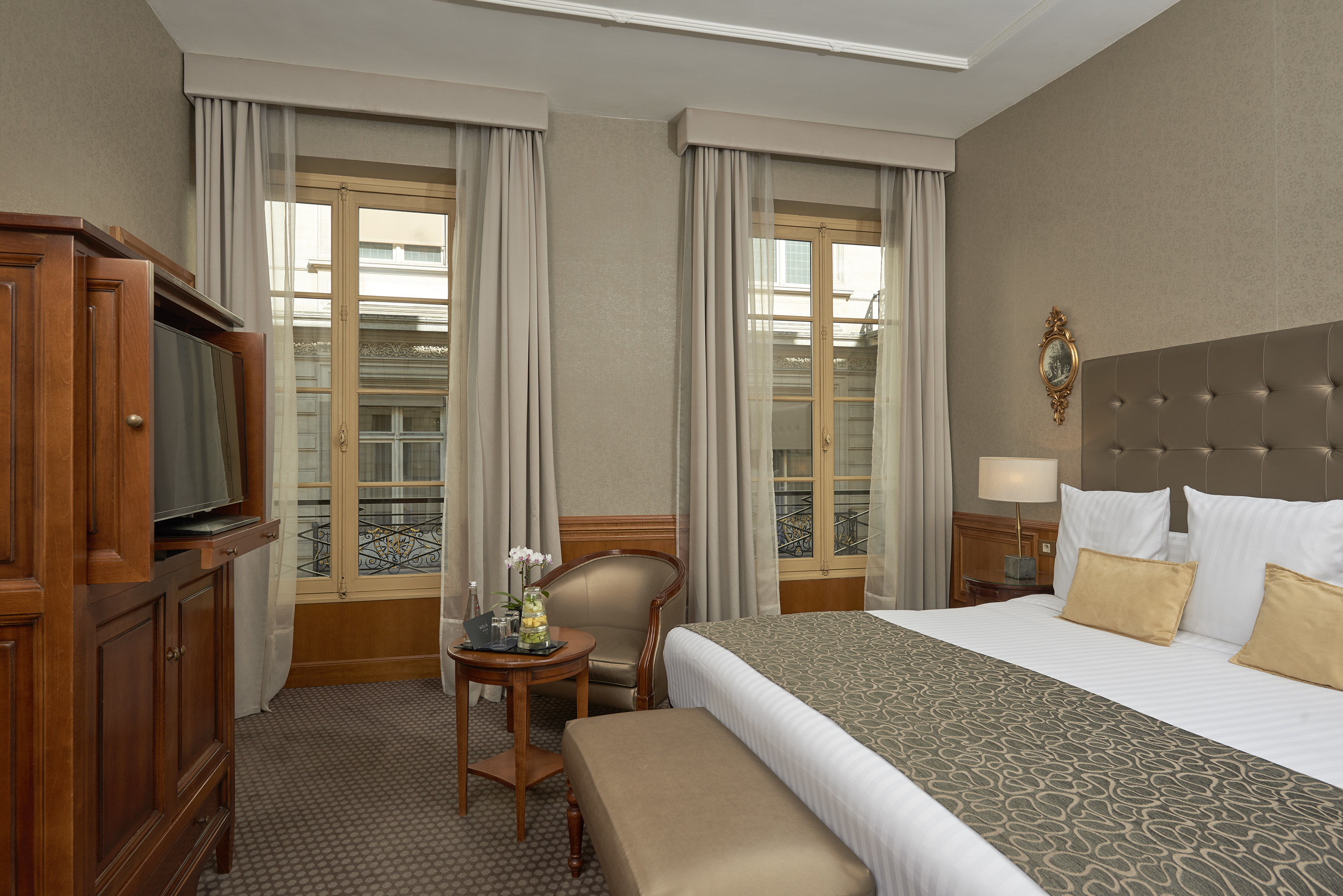 Hotel room with bed, large windows overlooking street, and wooden furniture.
