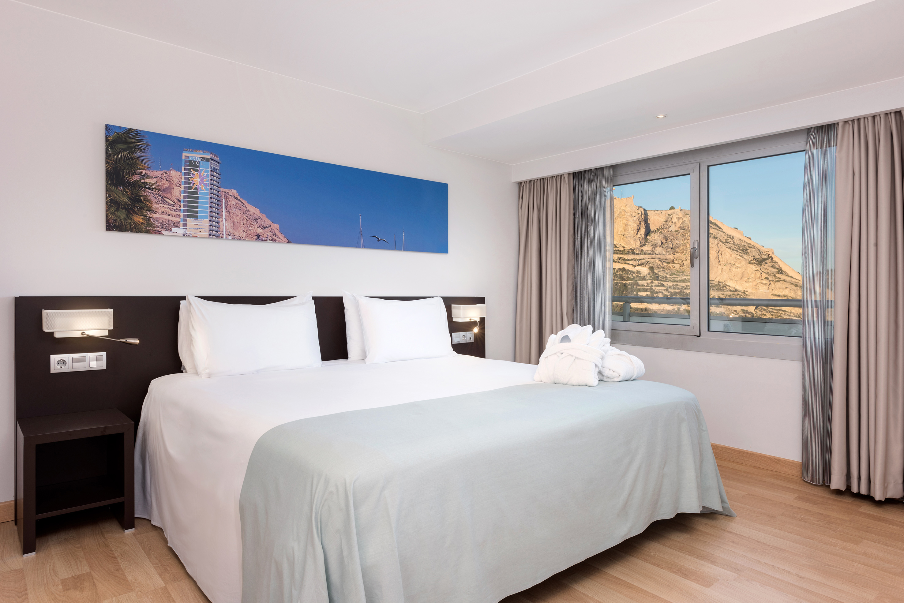 Modern hotel bedroom with king bed, white linens, mountain view, and bathrobes.
