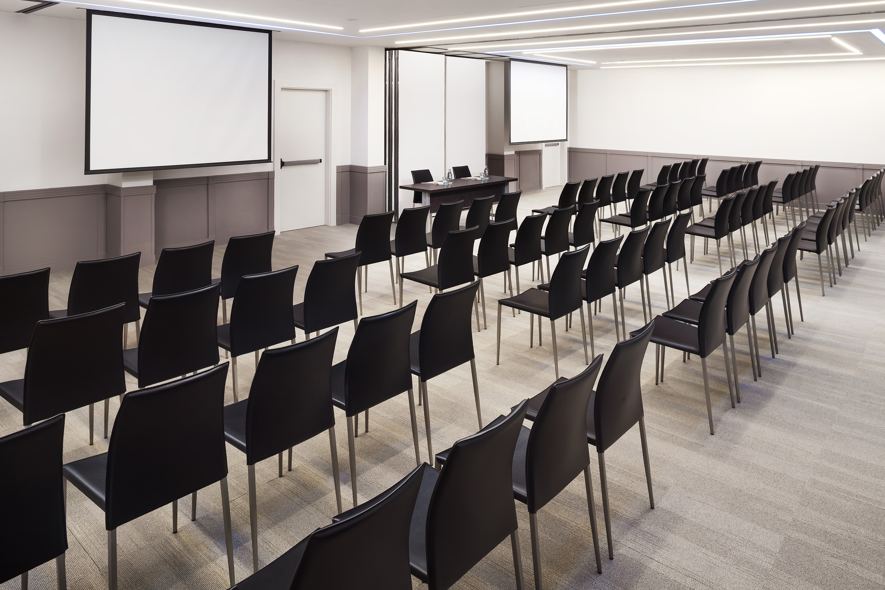 Empty modern conference room with black chairs and two projection screens.