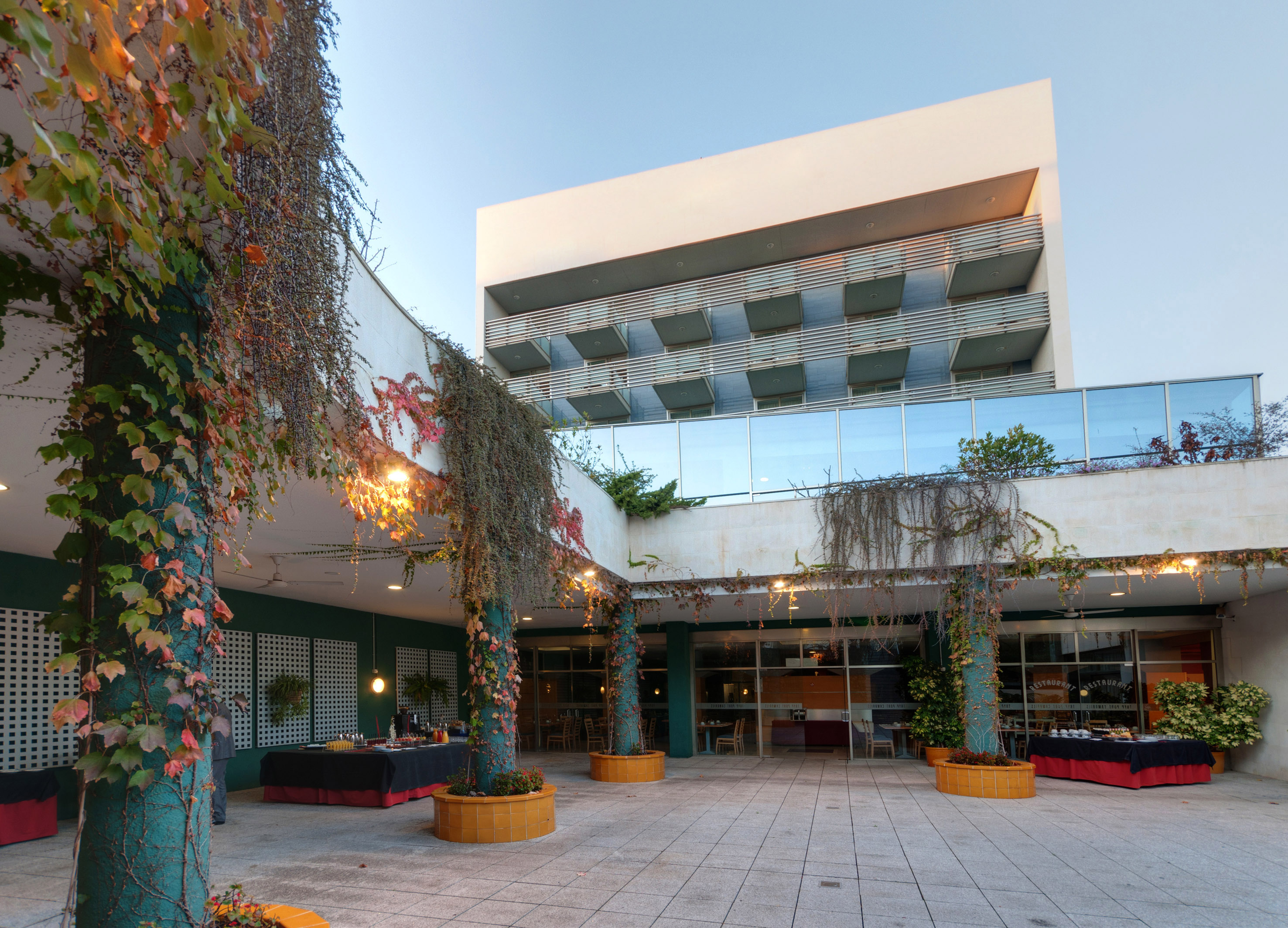 Hotel patio with ivy-covered pillars, outdoor dining setup, and modern building.