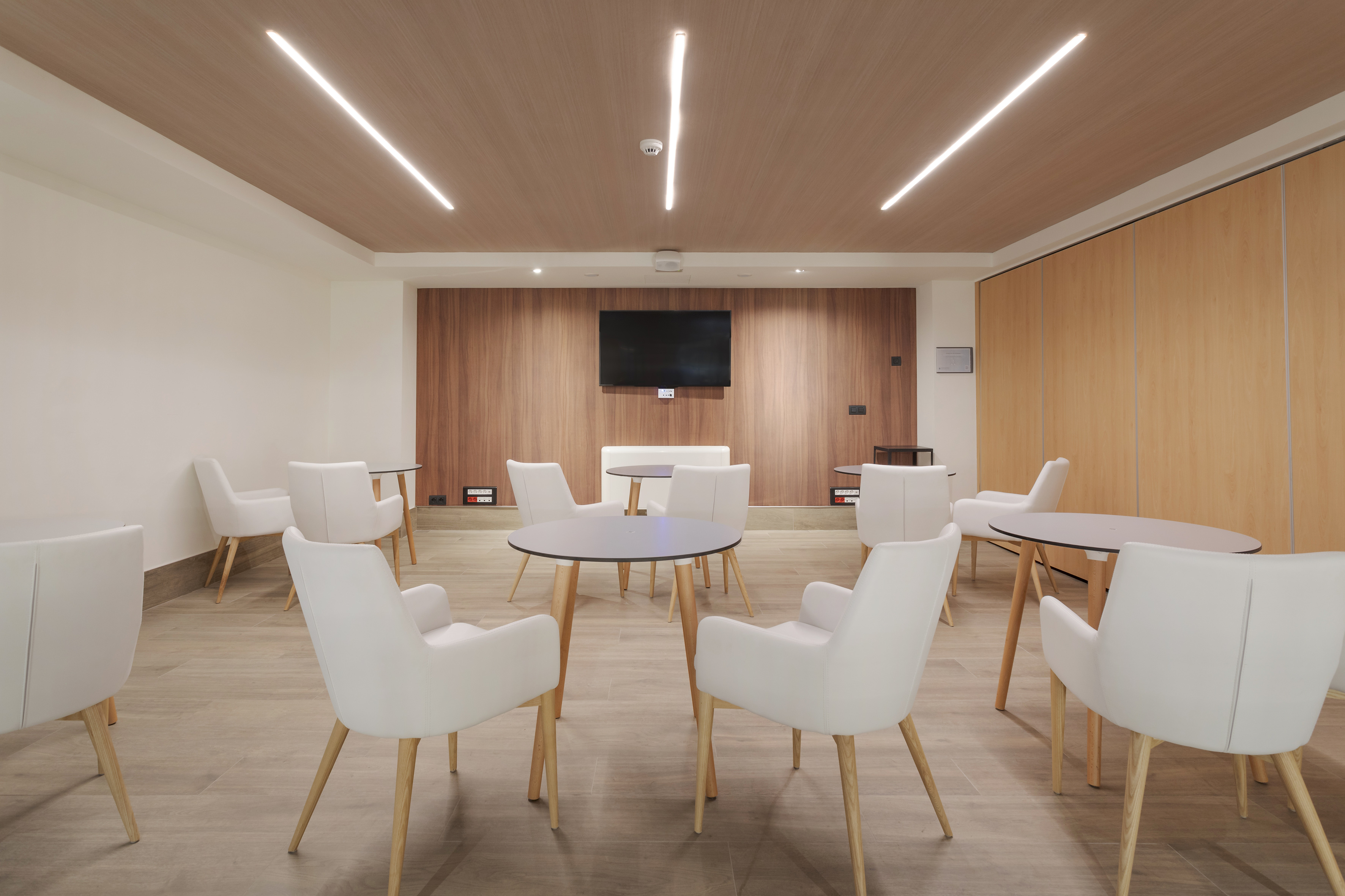 Modern lounge with white armchairs, wooden tables, and feature wall.