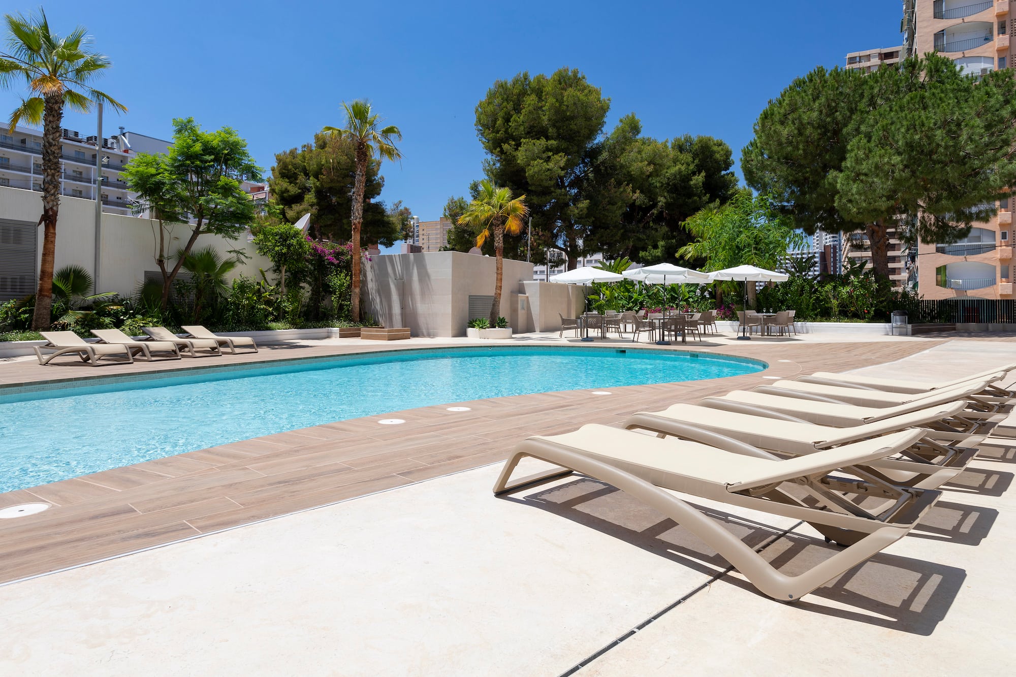 Resort swimming pool with sun loungers, palm trees, and outdoor seating area.