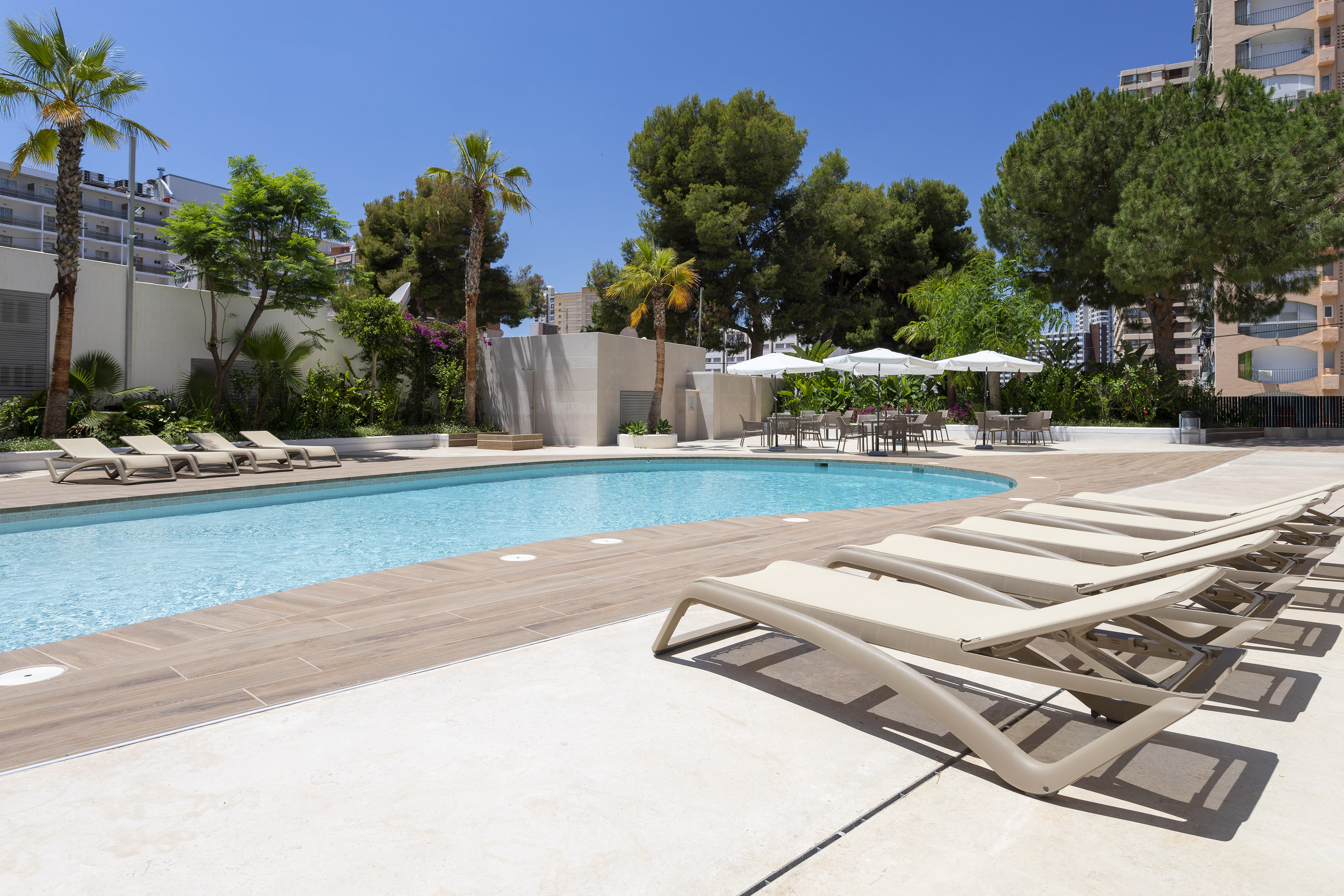 Resort swimming pool with sun loungers, palm trees, and outdoor seating area.