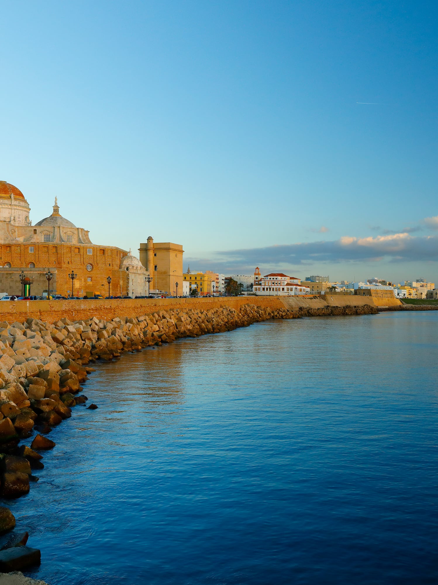 Cadiz Cathedral and waterfront city skyline, rocky breakwater, blue sea.
