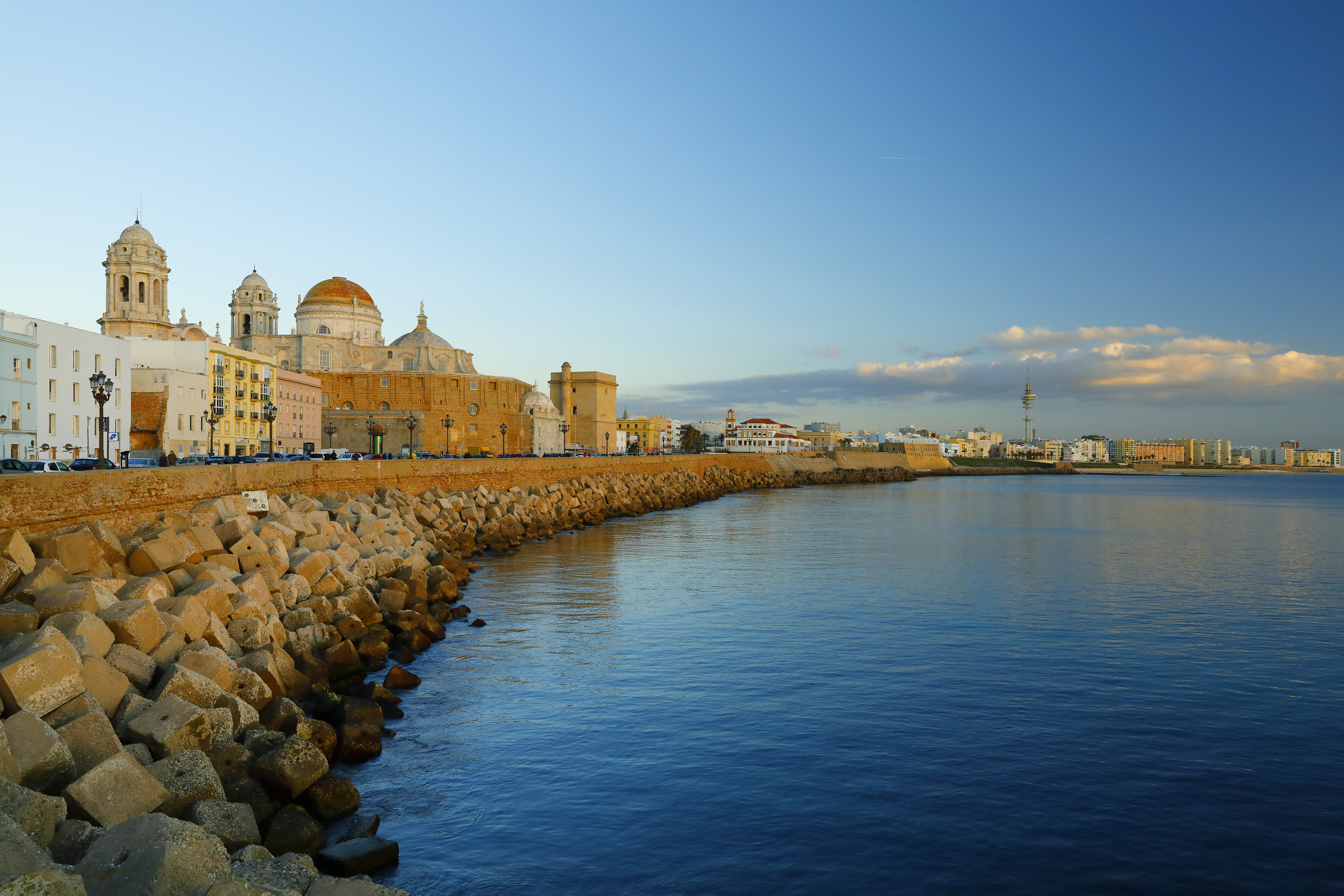 Cadiz Cathedral and waterfront city skyline, rocky breakwater, blue sea.