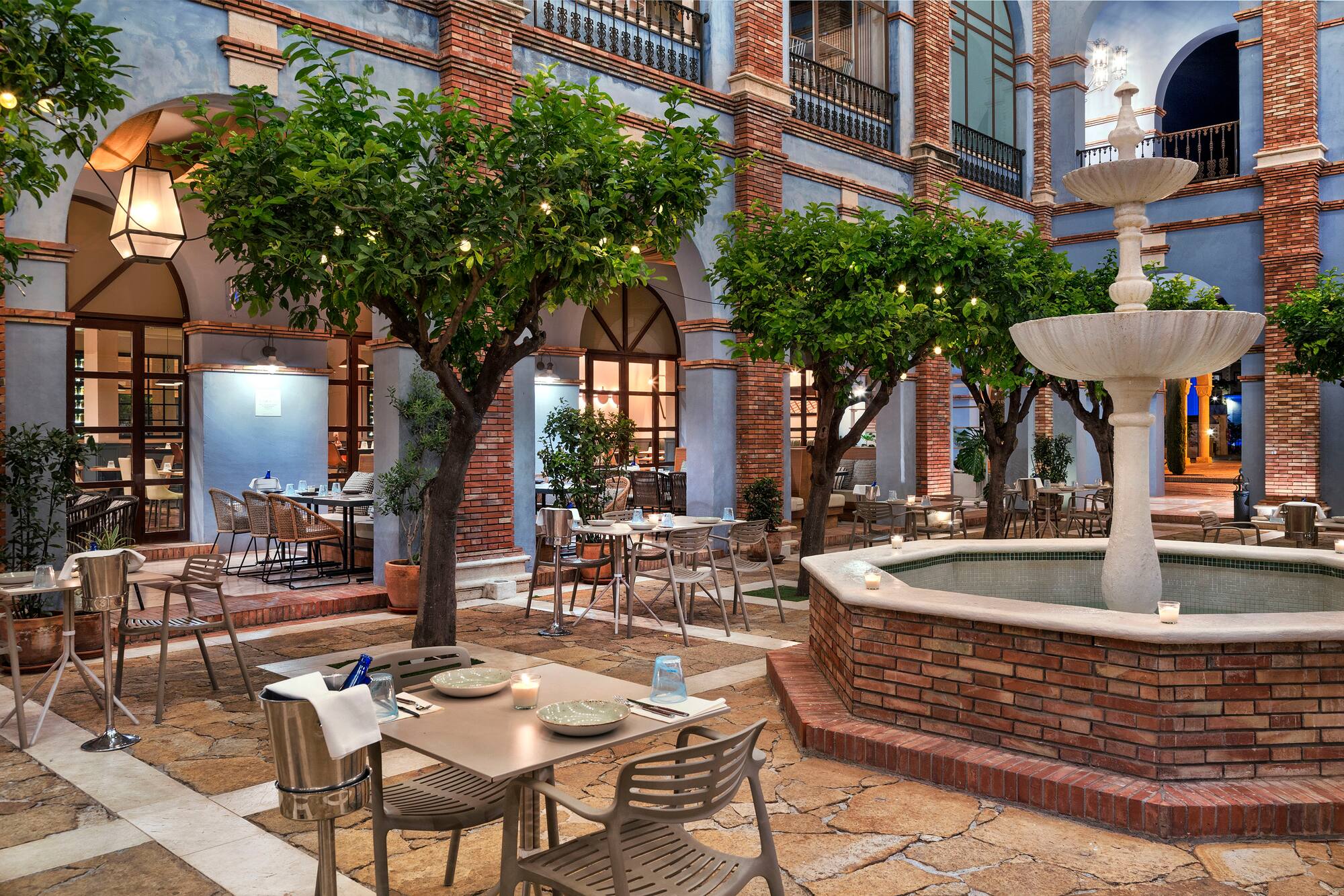 Mediterranean courtyard dining with fountain, lit trees, and outdoor tables.