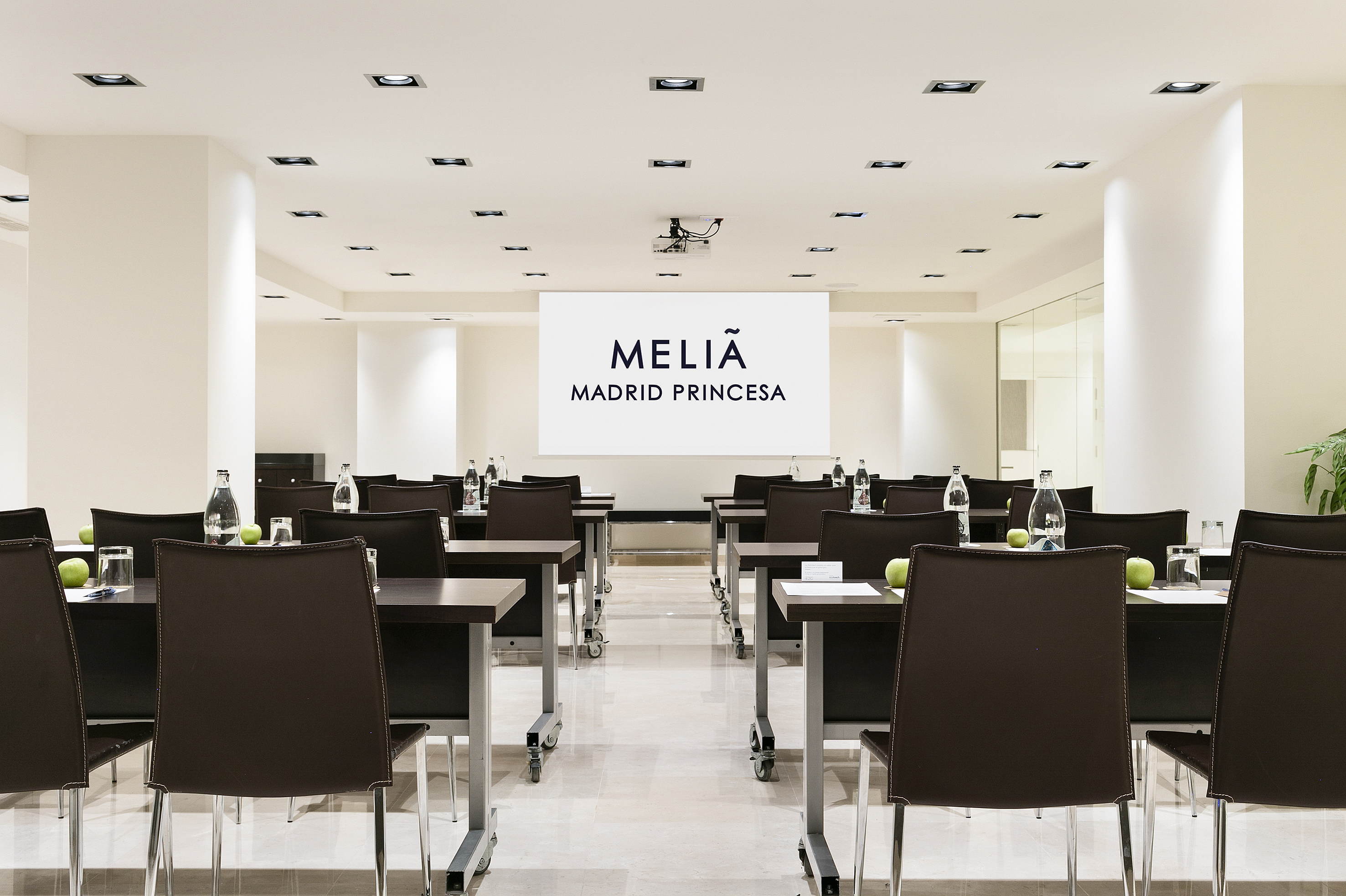 Meliã Madrid Princesa meeting space, projector screen, tables, and chairs.