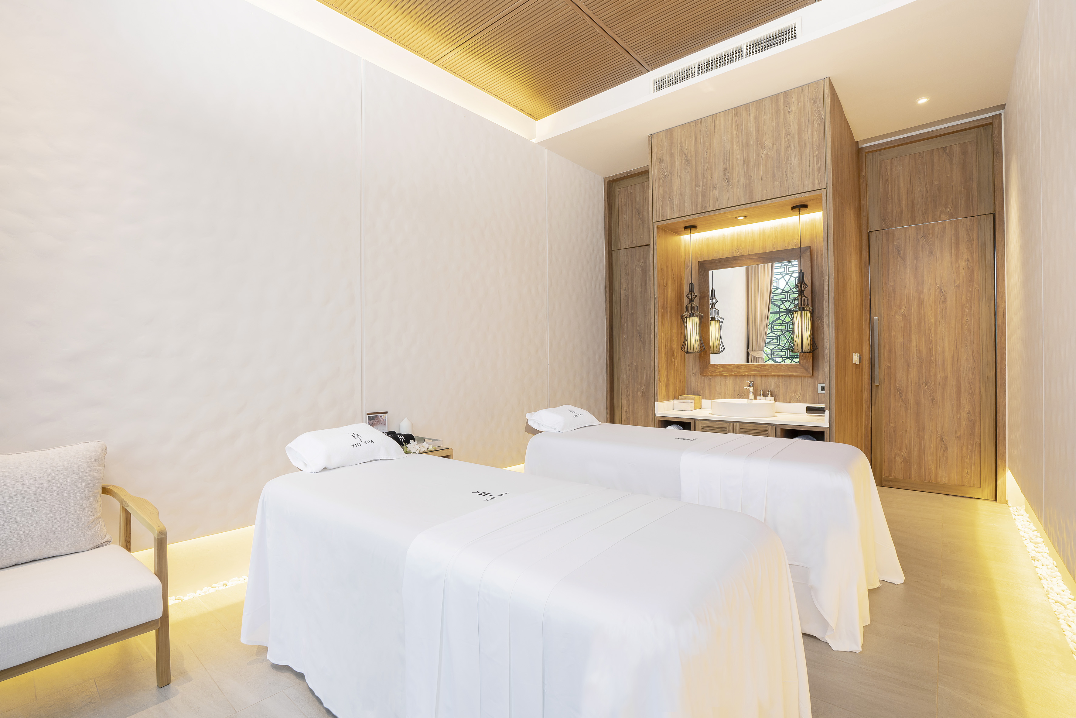 Luxury spa room with two white massage beds, wooden decor, and soft lighting.