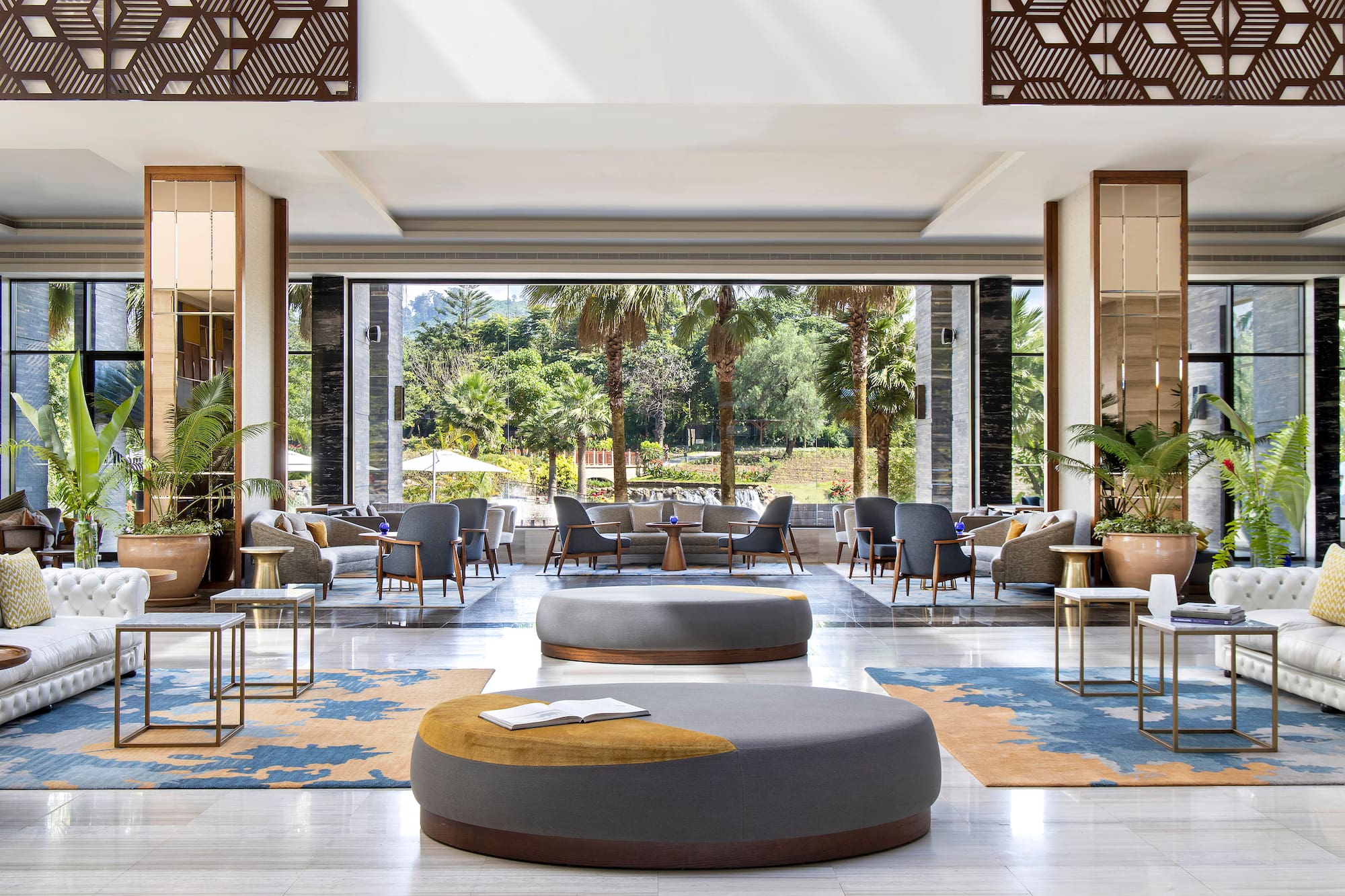 Modern hotel lounge, stylish seating, patterned rug, tropical garden view.