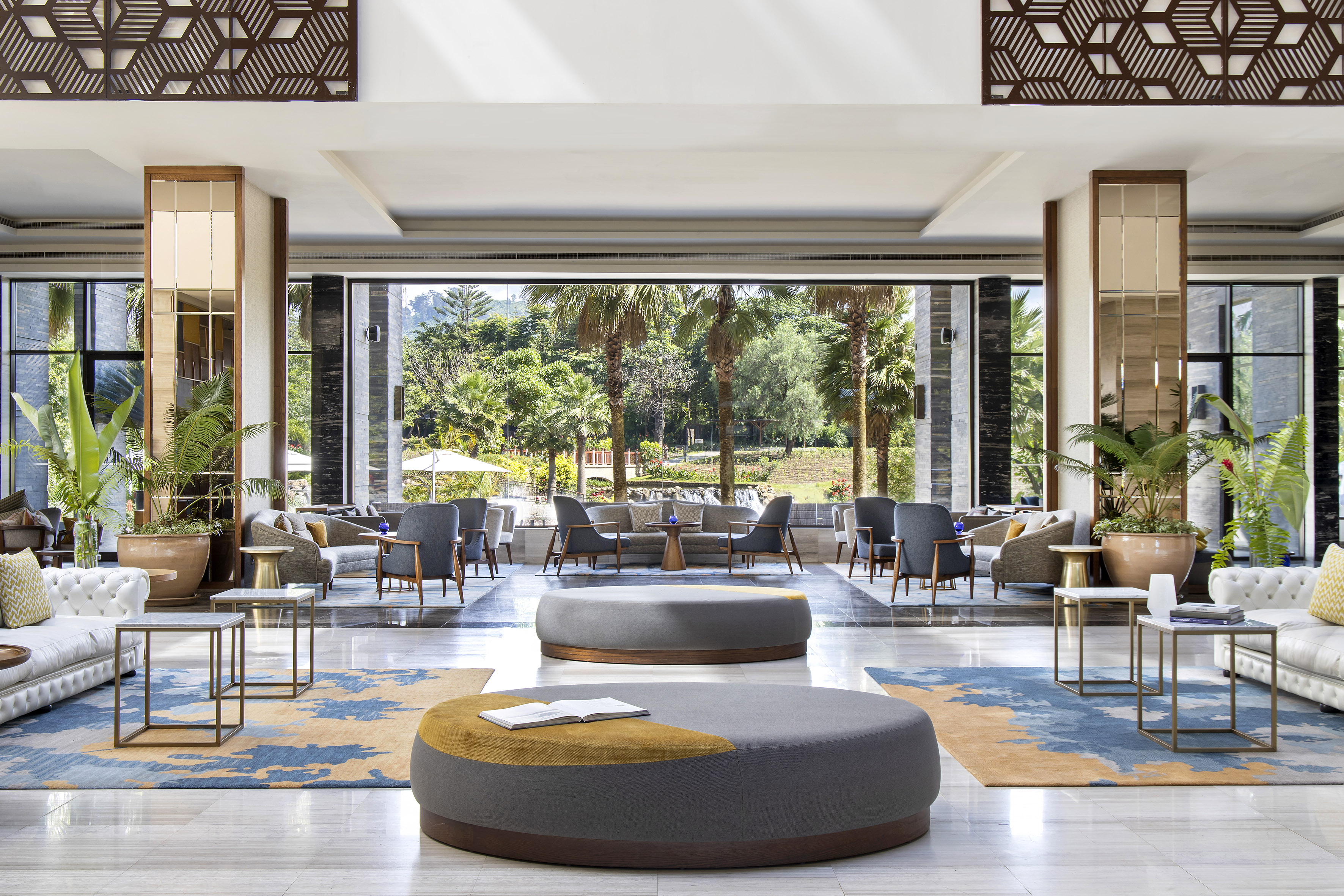 Modern hotel lounge, stylish seating, patterned rug, tropical garden view.