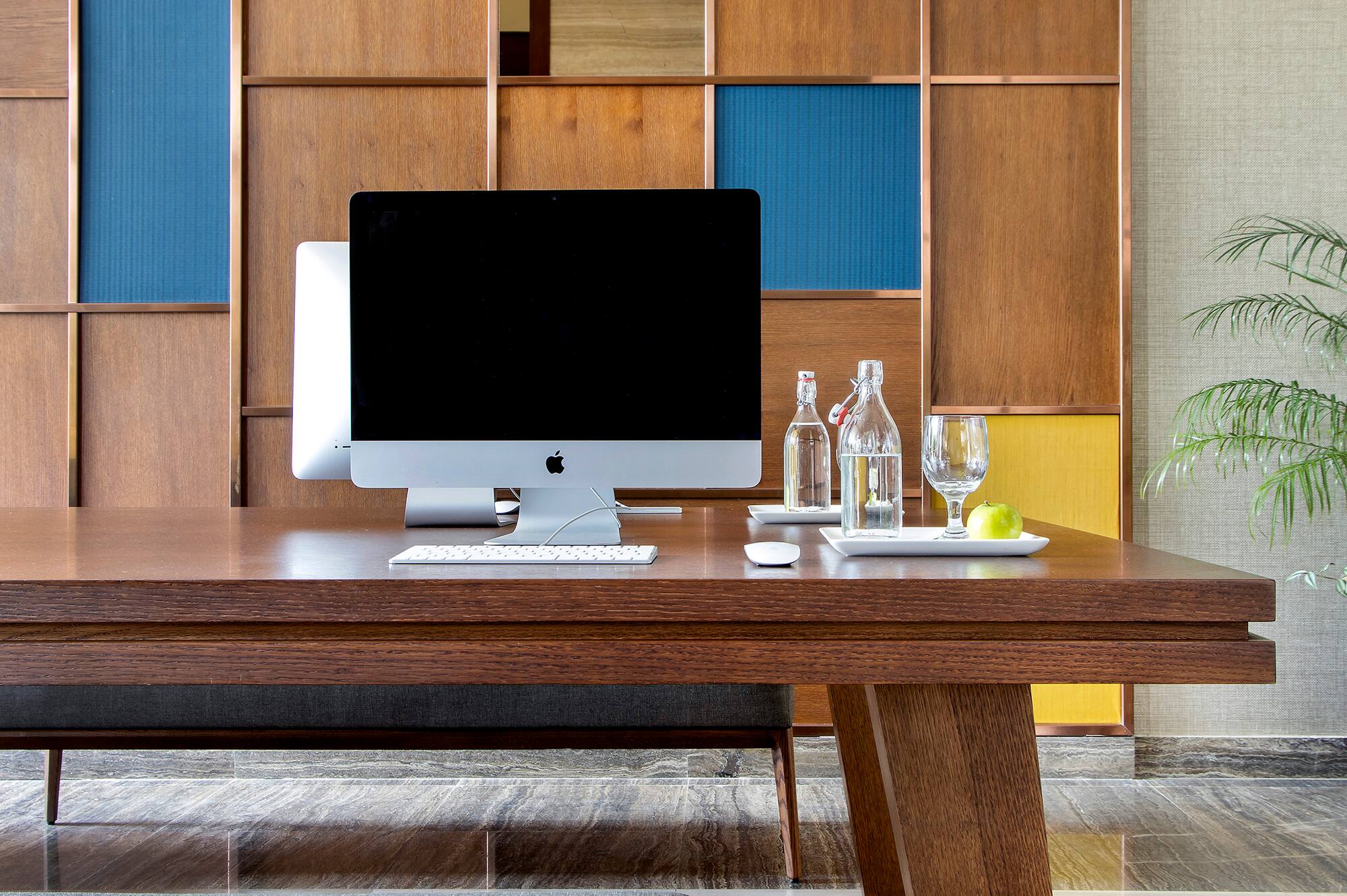 Modern office desk with iMac, wood panel wall, and upholstered bench.