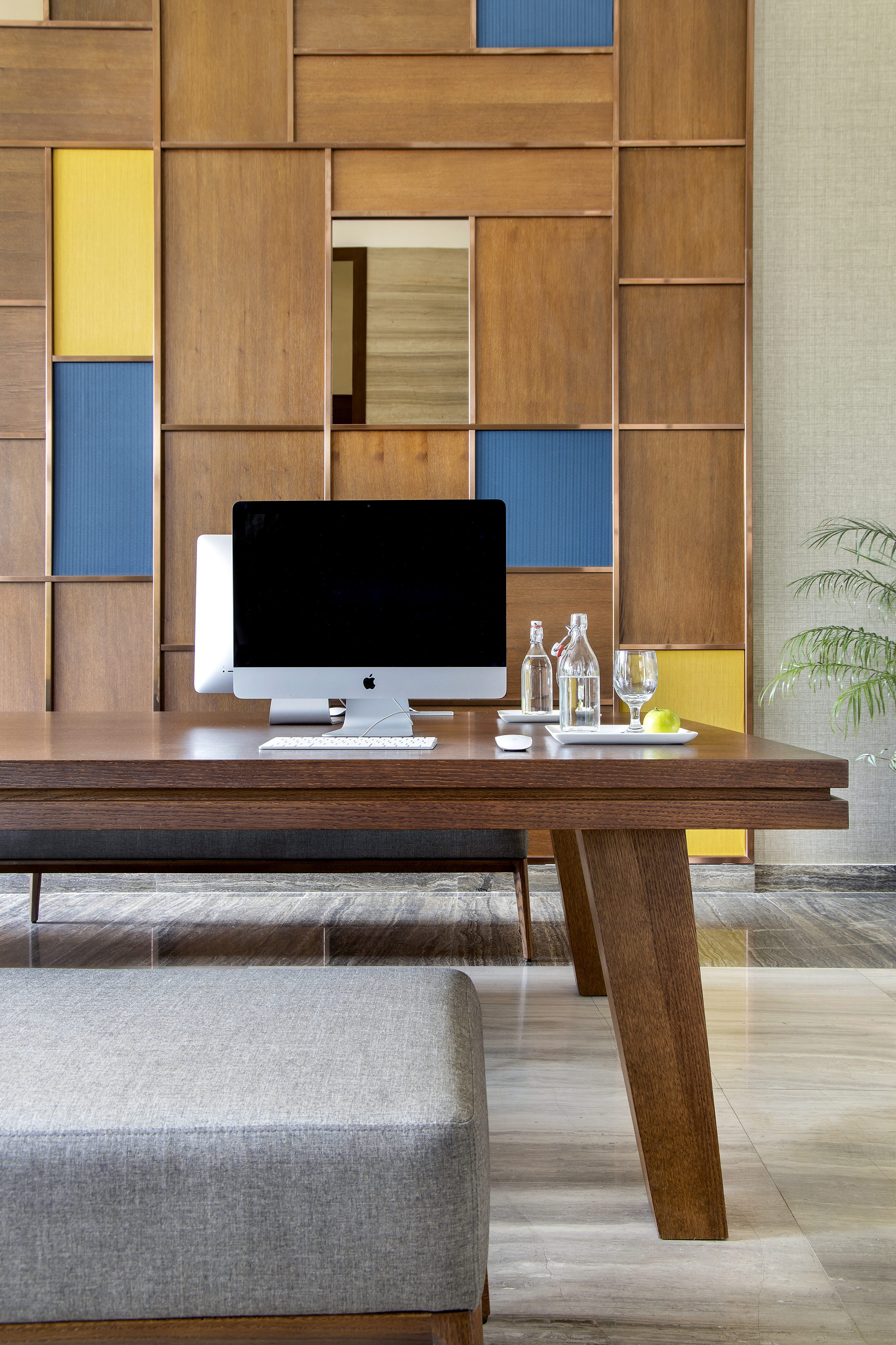 Modern office desk with iMac, wood panel wall, and upholstered bench.