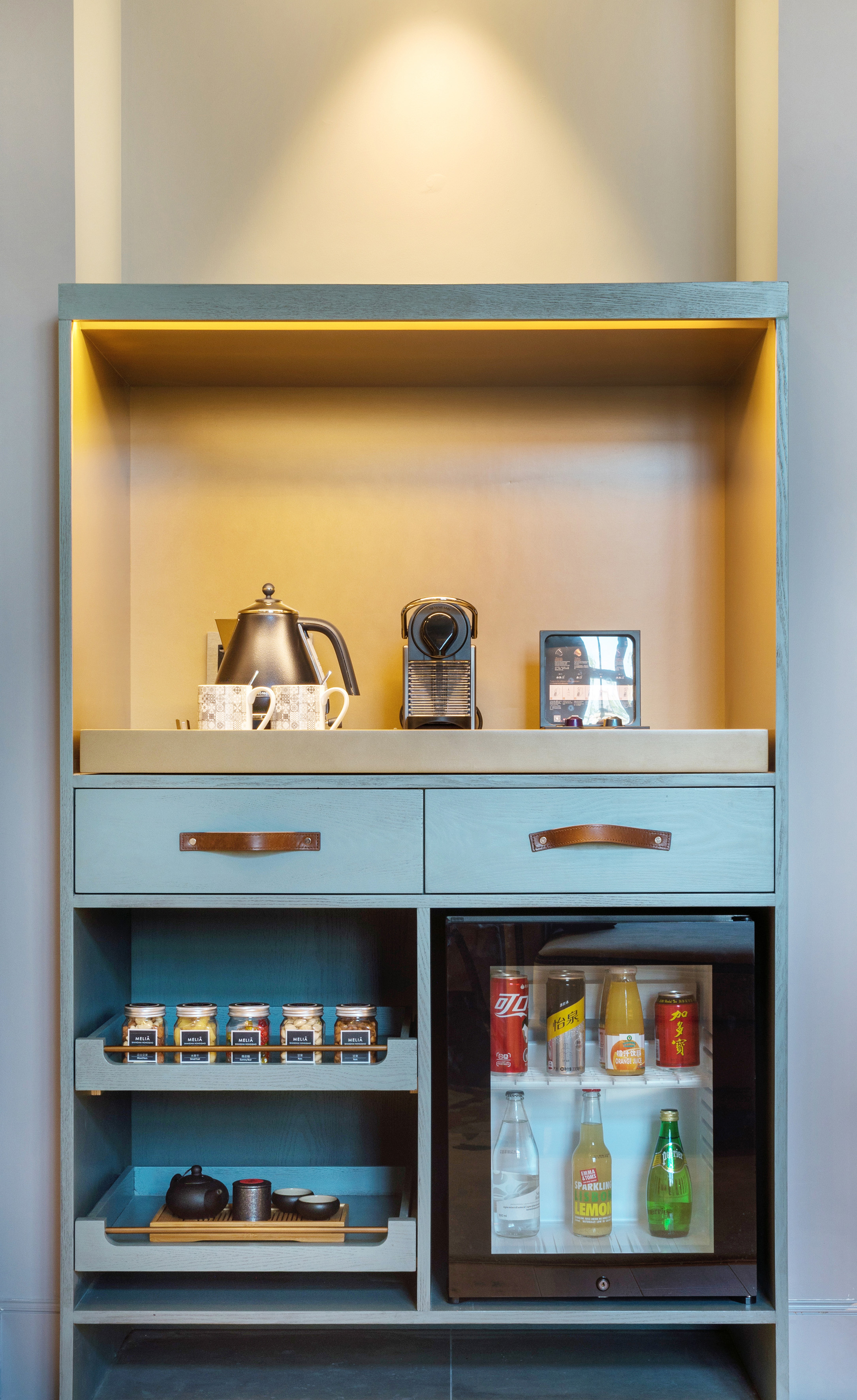 Hotel minibar cabinet with Nespresso, kettle, tea set, snacks, and drinks.