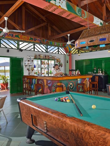 a pool table in a room with a bar and a man behind it
