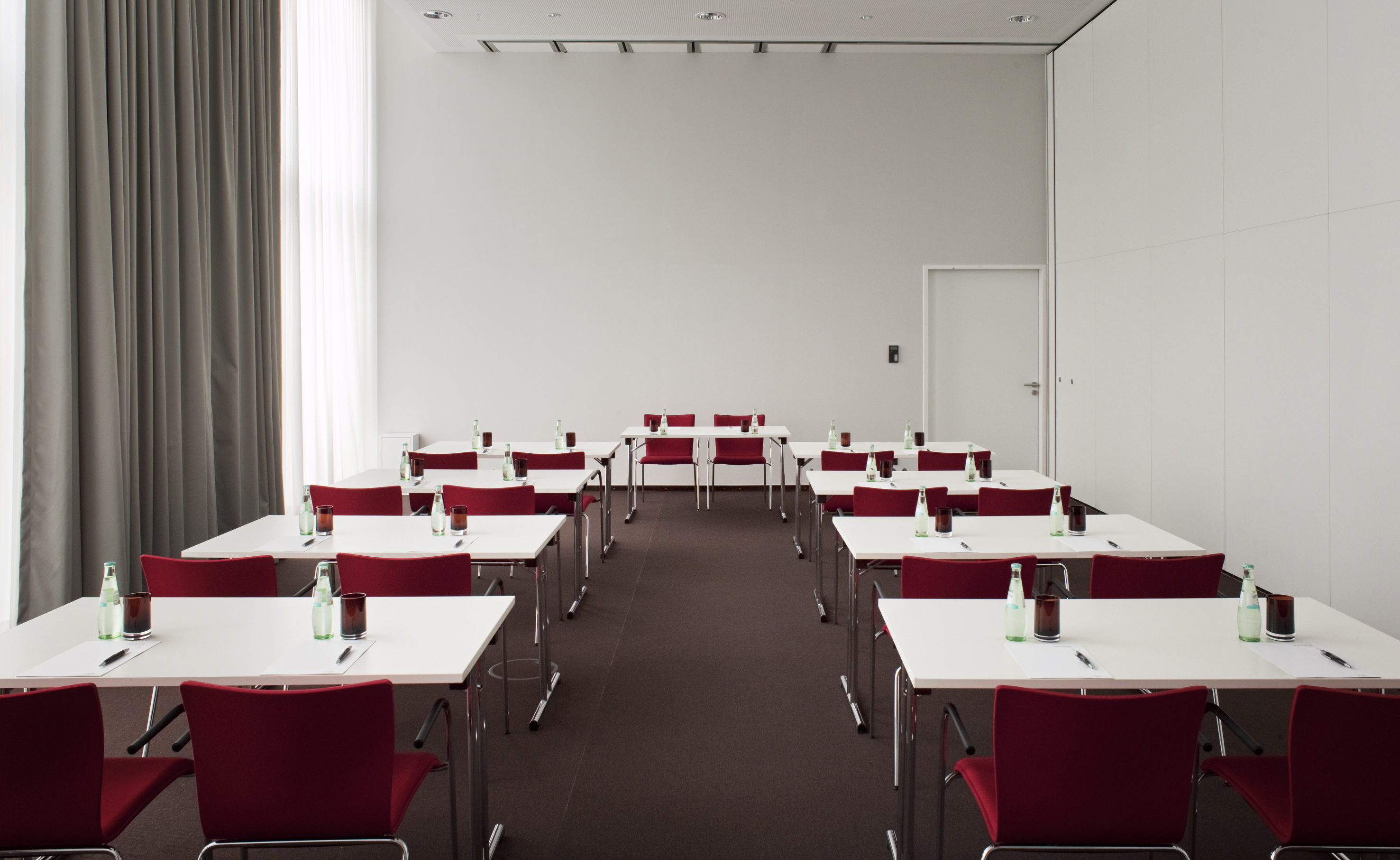 Modern meeting room setup with white tables, red chairs, bottled water.