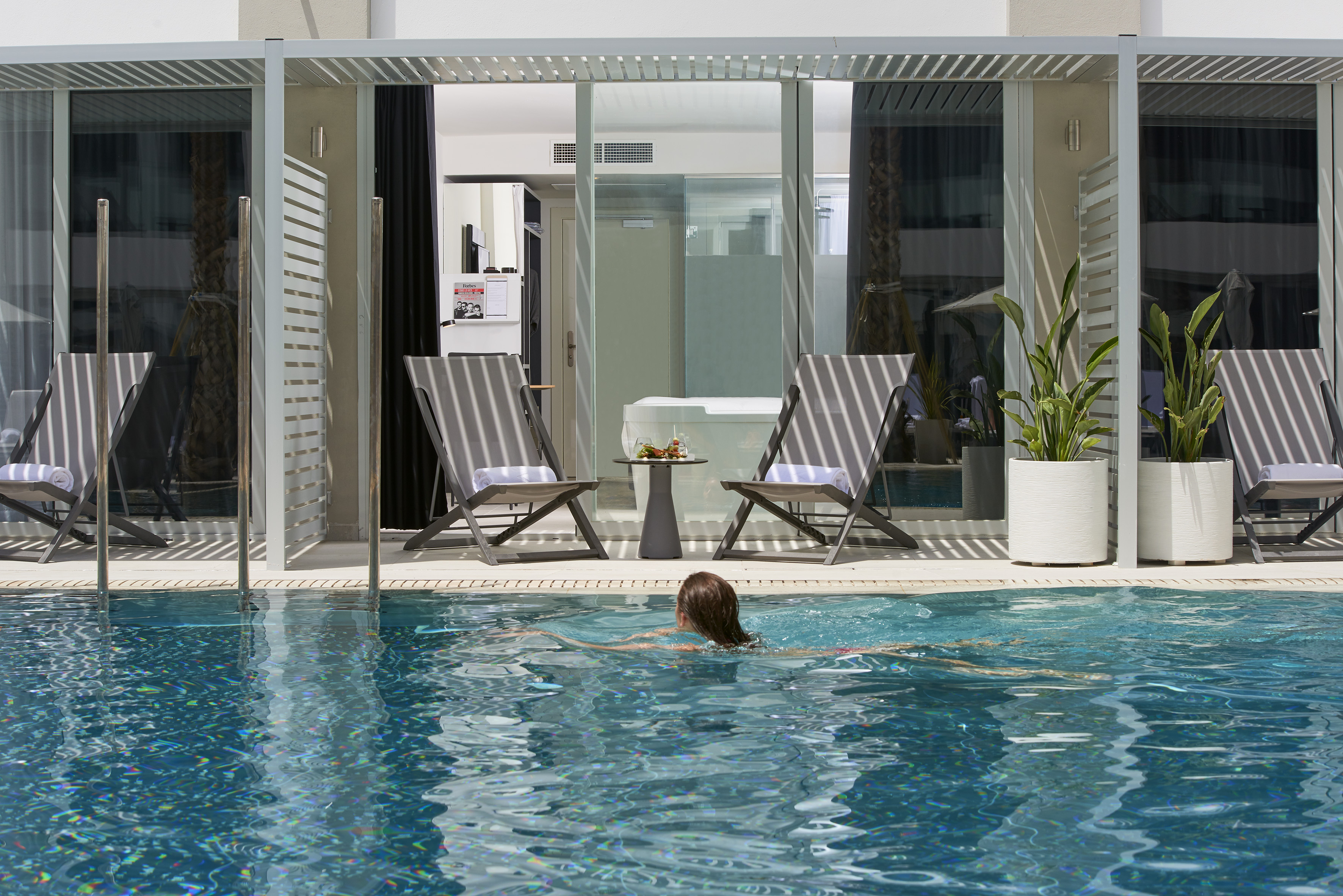 Woman swimming in private pool, modern hotel suite terrace with loungers.