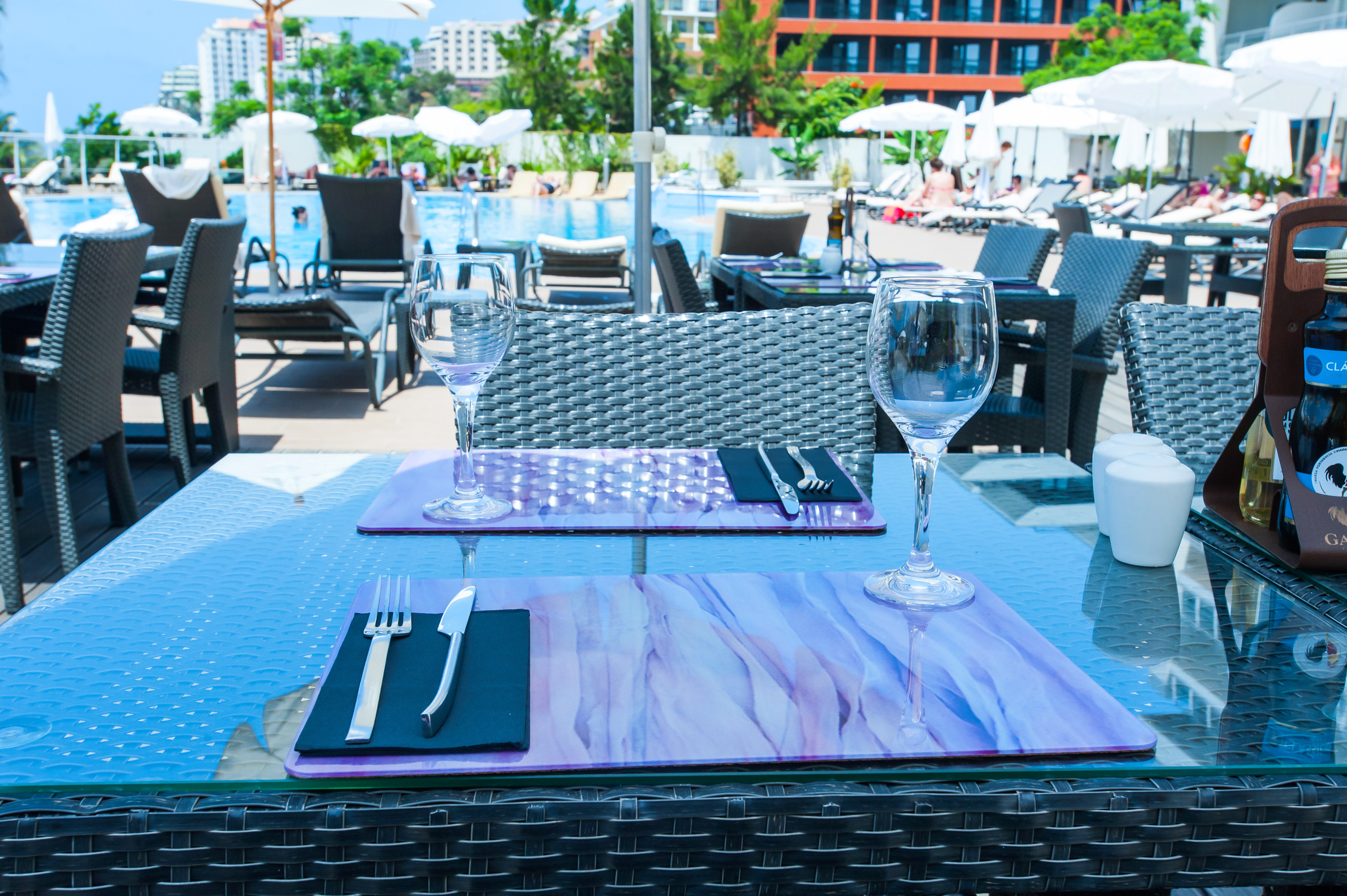 Poolside restaurant table set for two with wine glasses at a luxury resort.