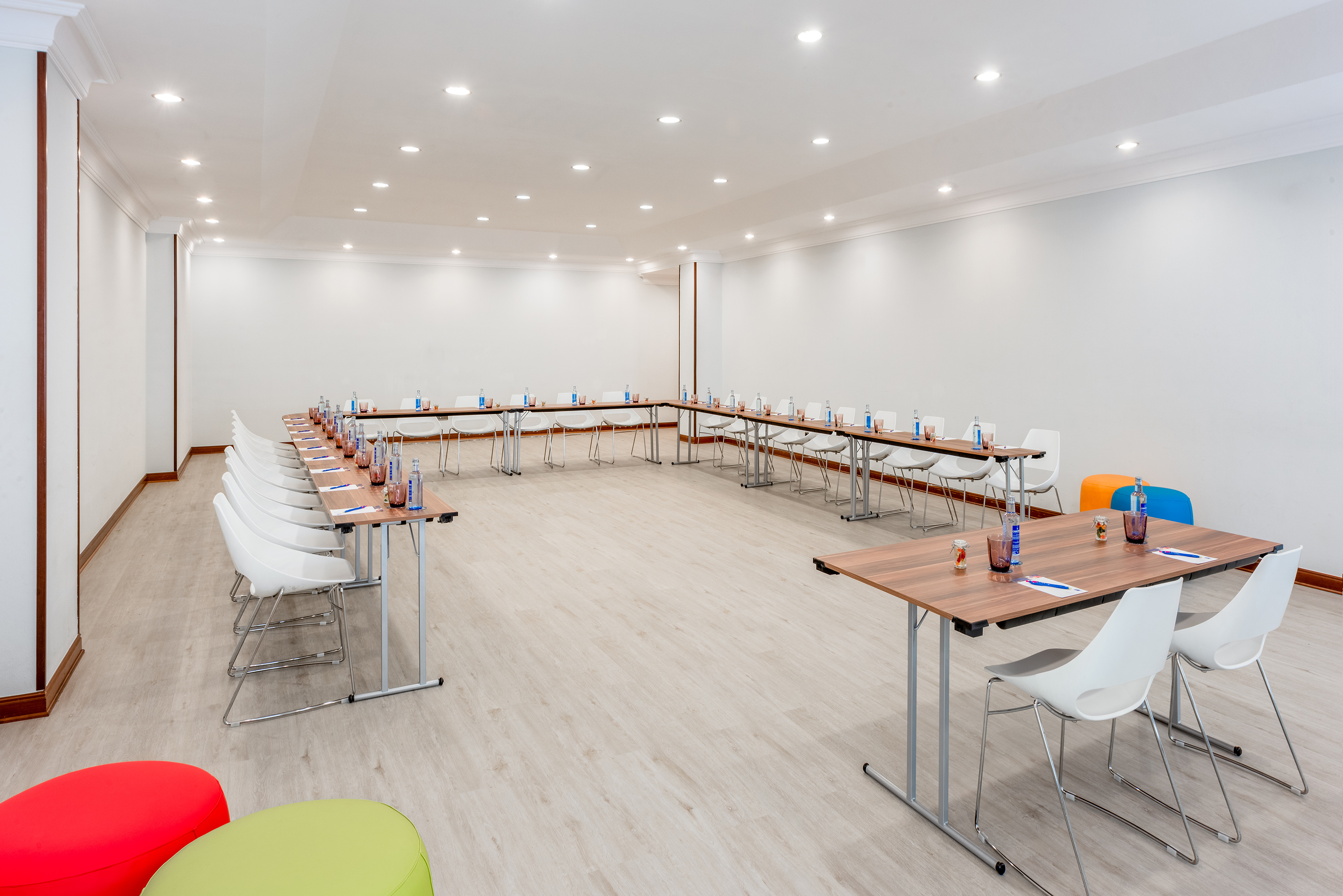 Modern U-shape meeting room setup with tables, white chairs, and bright lighting.