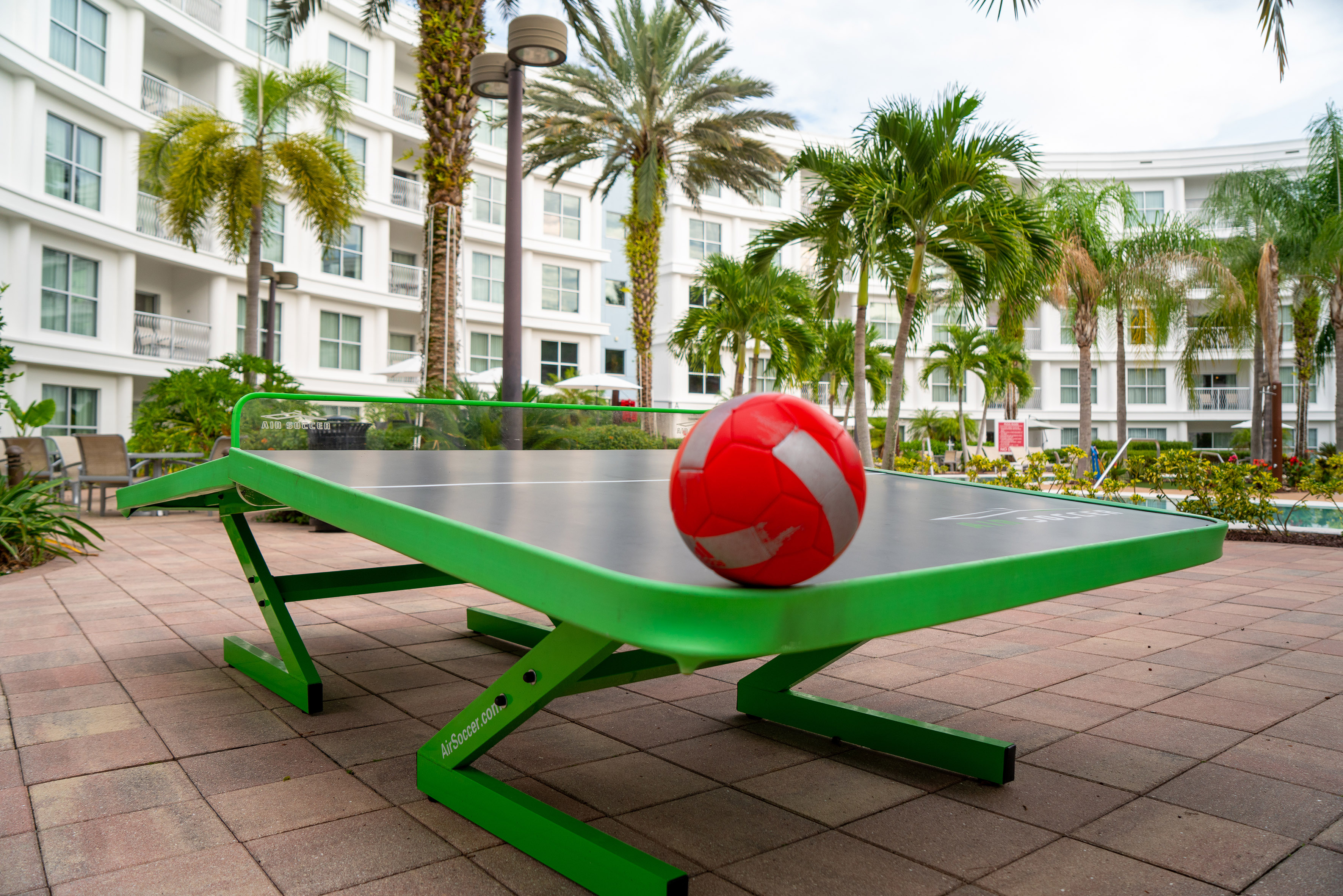Red soccer ball on green Air Soccer table outdoors at a tropical resort.